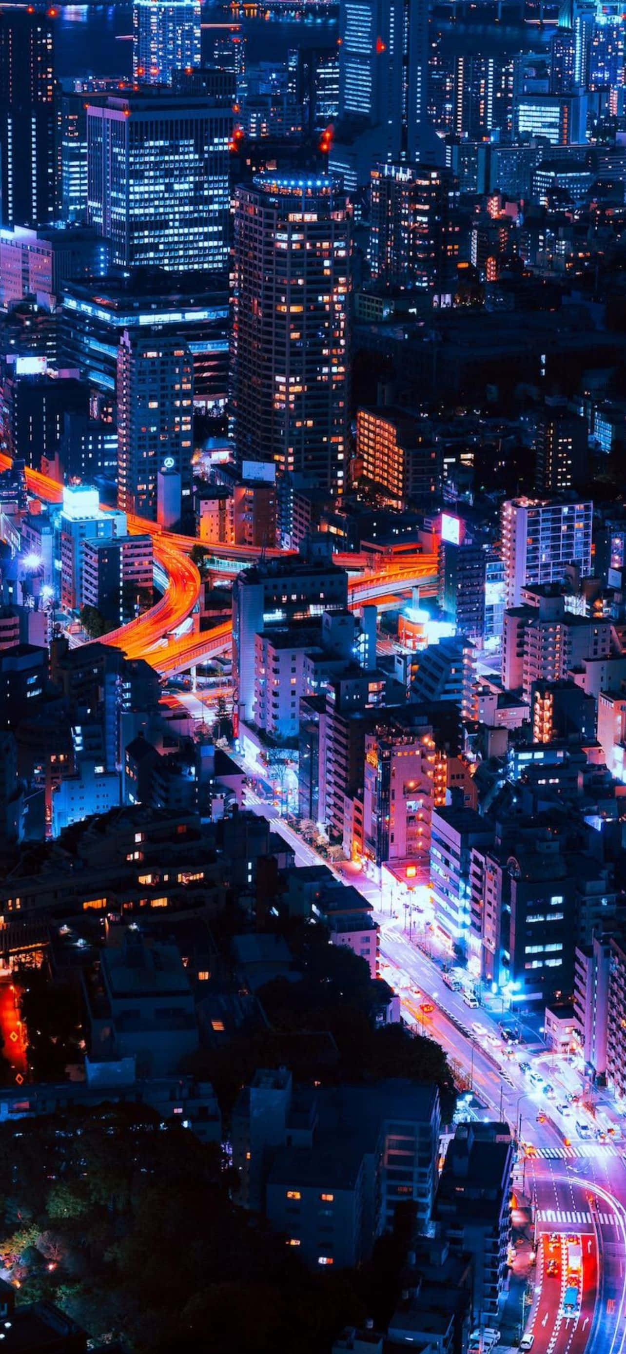 酷炫iPhone 桌布 壁紙 — 夜晚霓虹燈照亮城市景觀的鳥瞰圖，閃爍的摩天大樓和充滿活力的交通痕跡。
