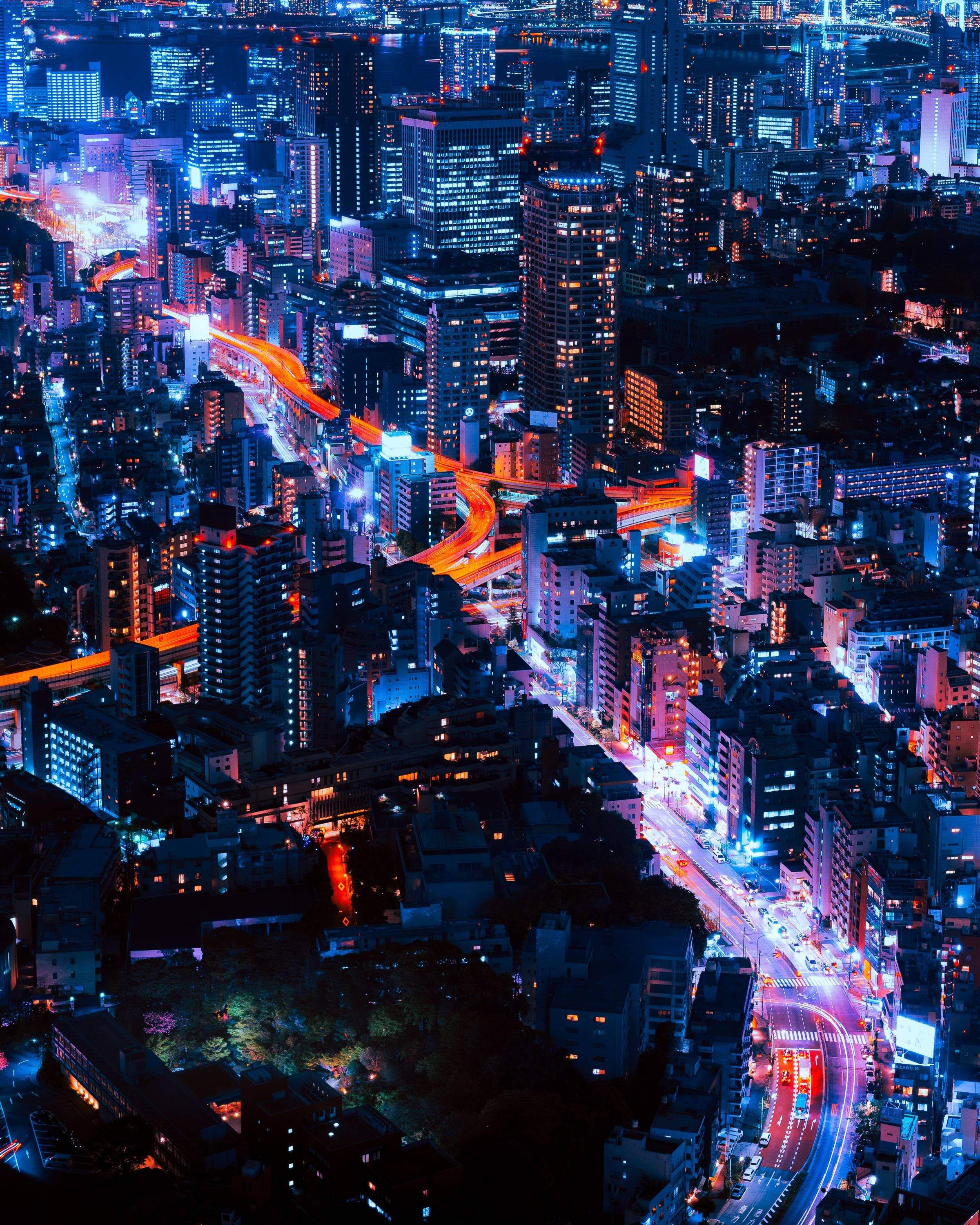 東京 桌布 壁紙 — 夜晚霓虹燈照亮城市的鳥瞰圖，有發光的藍色摩天大樓和橙色的車流燈光軌跡。