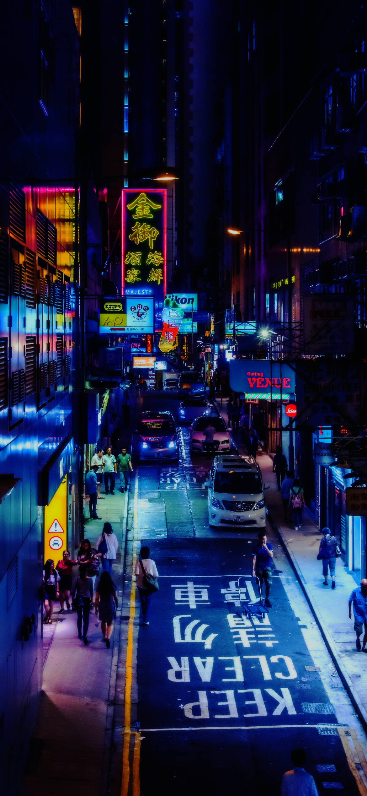City At Night 桌布 壁紙 — 夜晚霓虹燈照亮的城市小巷，發光招牌倒映在濕漉漉的路面，行人經過停放的車輛。