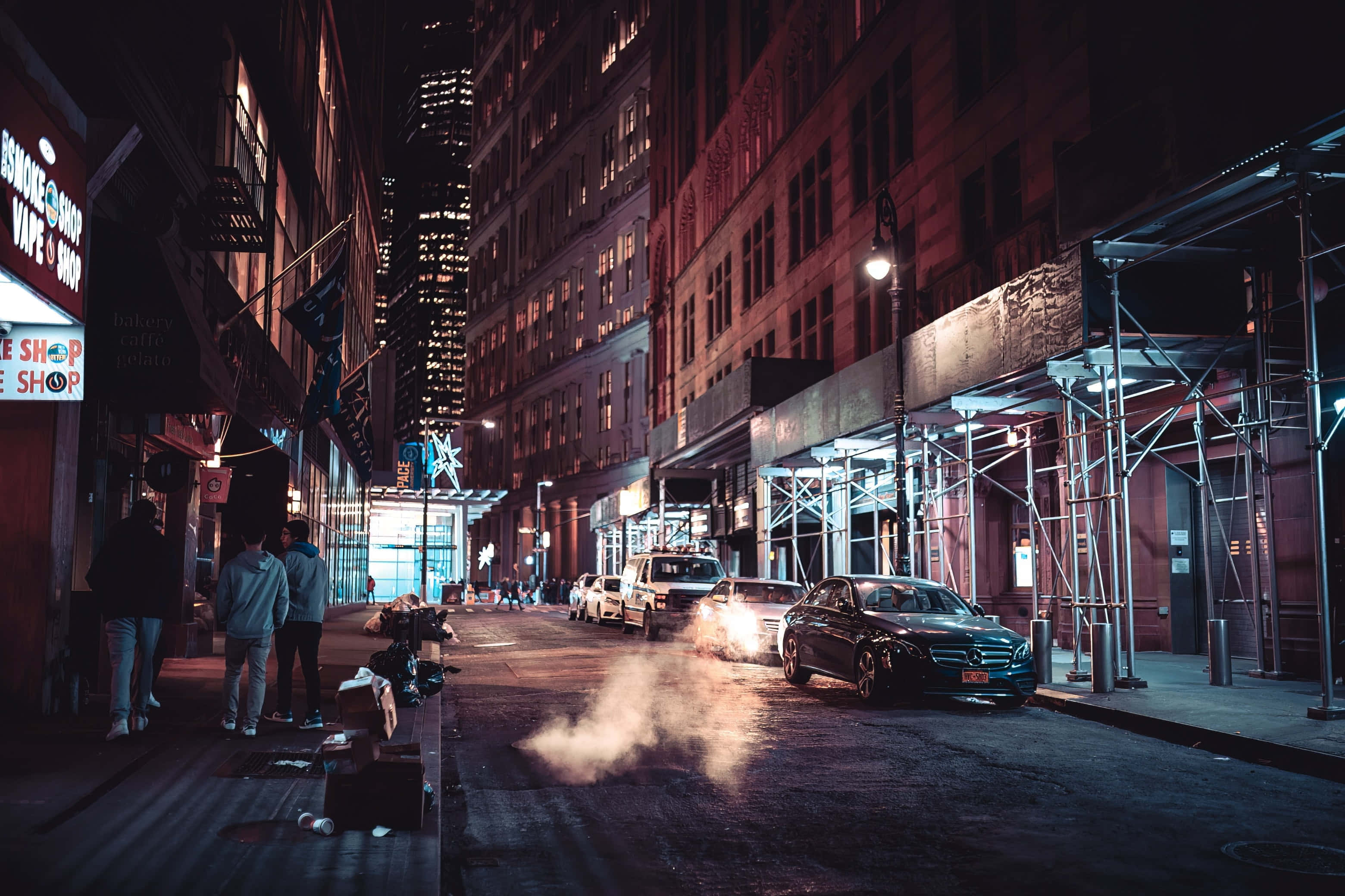 街頭 桌布 壁紙 — 夜晚霓虹燈照亮的城市小巷，行人走過停放的汽車和磚造建築的鷹架。