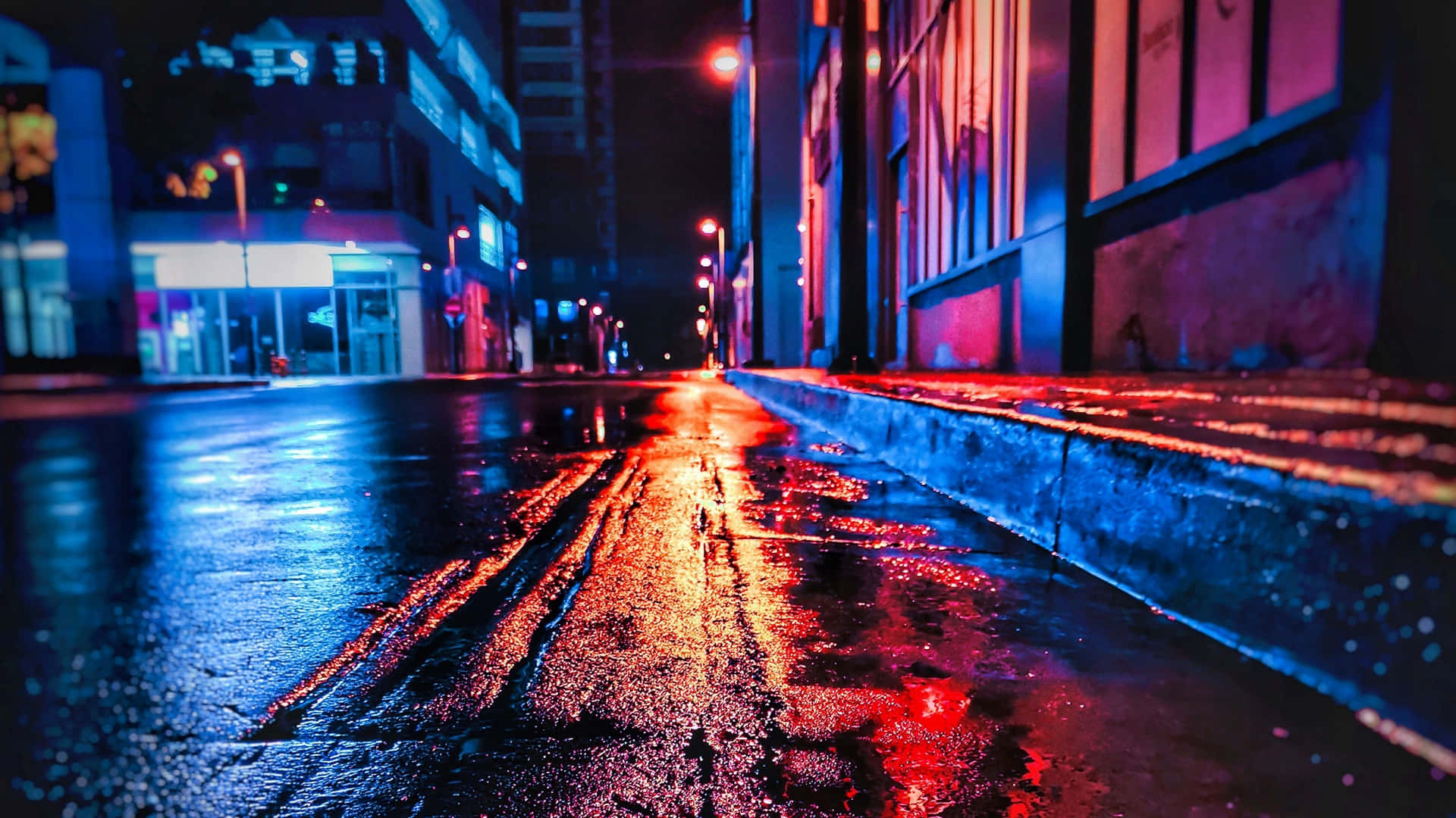 Neon City Aesthetic 桌布 壁紙 — 夜晚霓虹燈照亮的城市街道，濕漉漉的路面反射著建築物和路燈的鮮豔紅藍燈光。