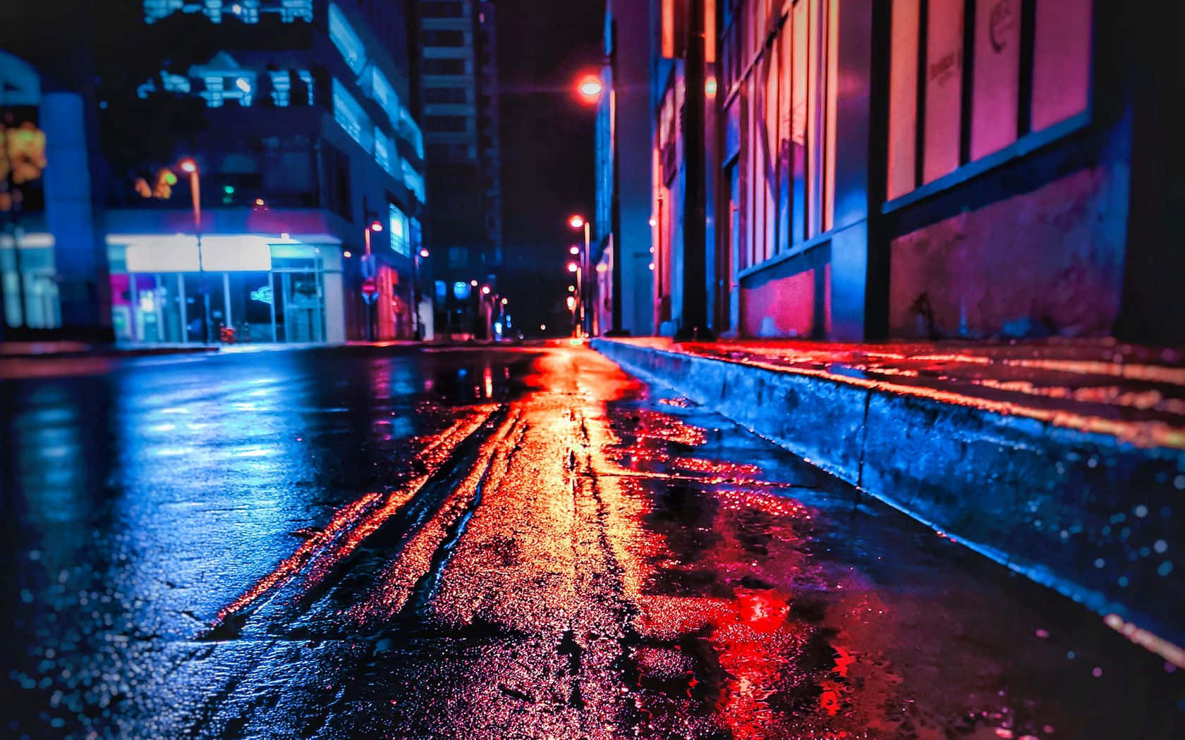 桌布 壁紙 — 夜晚霓虹燈照亮的城市街道，濕漉漉的路面反射著建築物和路燈的鮮豔紅藍燈光。