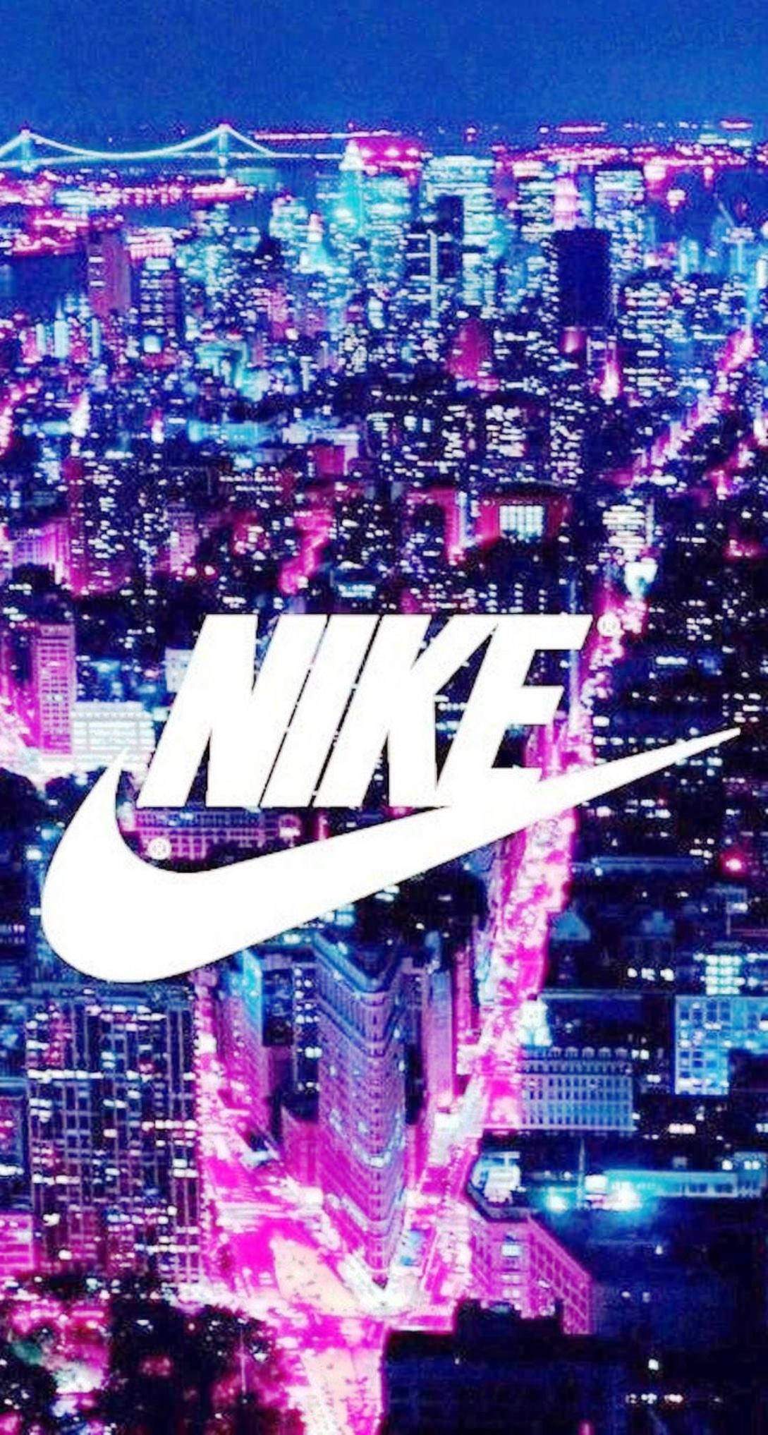 Nike iPhone 桌布 壁紙 — 夜晚霓虹燈閃爍的城市景觀，一個大型白色Nike標誌疊加在發光的粉紅色和藍色摩天大樓和街道上。