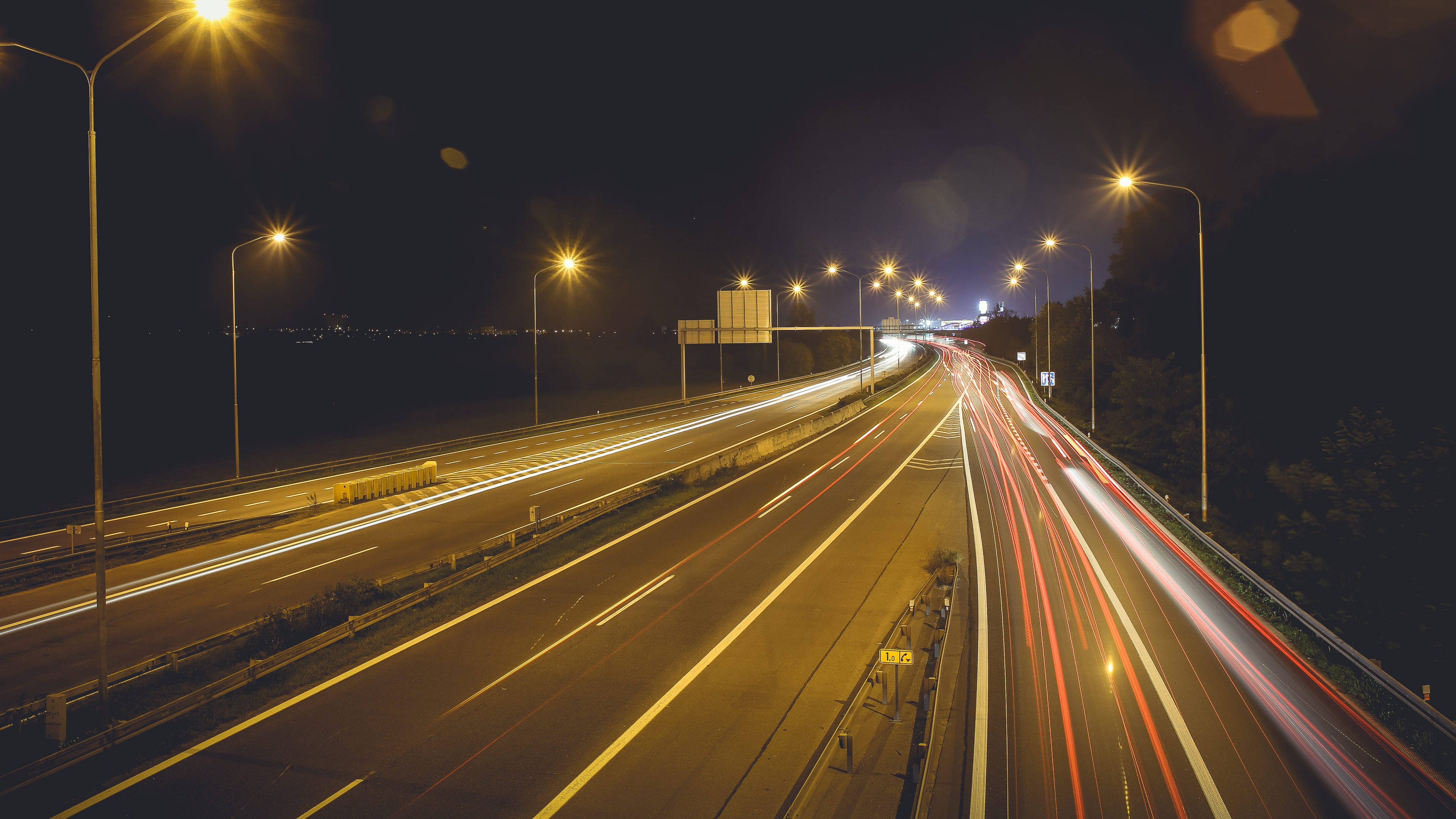 Road 桌布 壁紙 — 夜晚高速公路的長時間曝光照片，顯示在發光路燈下行駛車輛的紅色和白色燈光軌跡。