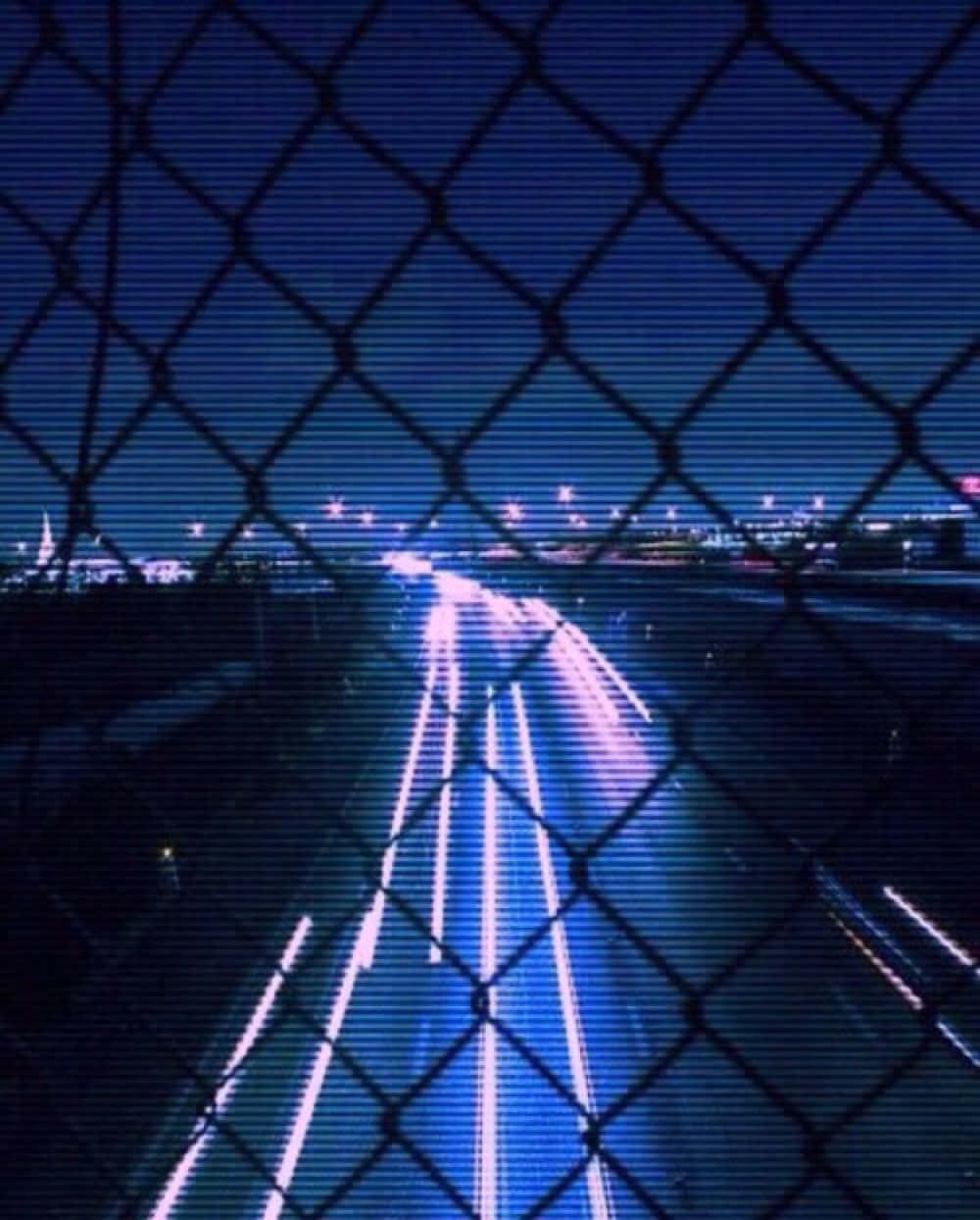 攝影 桌布 壁紙 — 夜晚高速公路透過鐵絲網圍欄觀看，帶有行駛車輛留下的藍色和白色光跡。