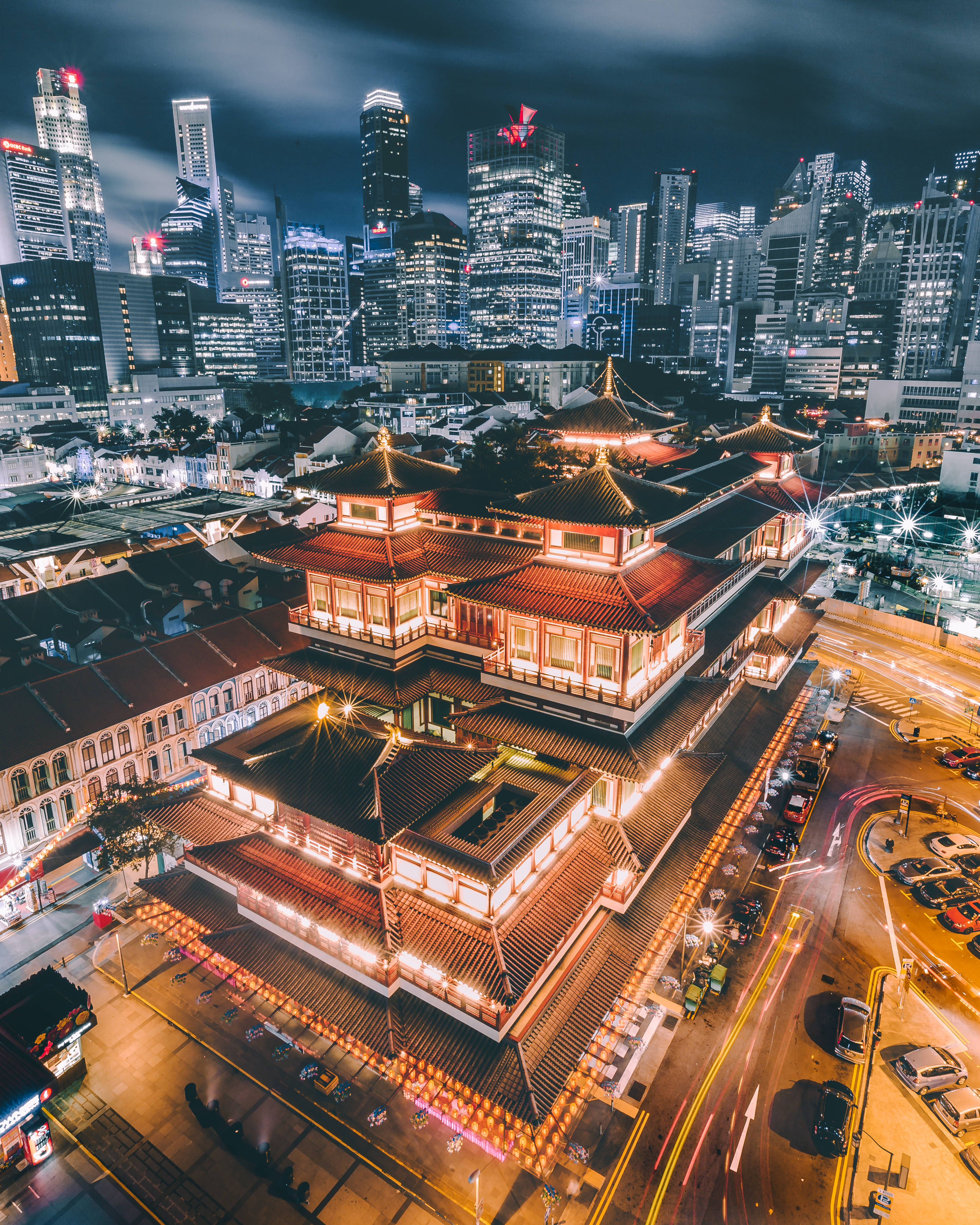 Singapore 桌布 壁紙 — 夜晚鳥瞰一座發光的傳統寺廟，紅色屋頂，坐落在現代摩天大樓和光跡之中。