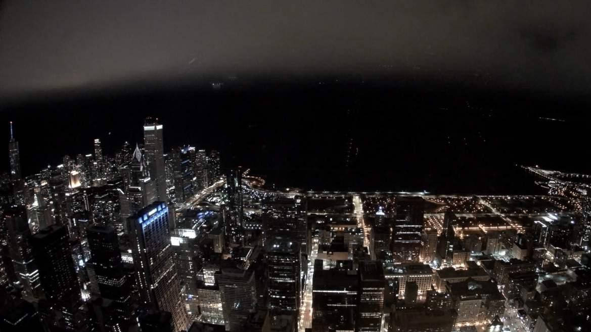 Chicago Skyline 桌布 壁紙 — 夜晚鳥瞰廣闊的城市景觀，摩天大樓和街道在陰暗多雲的天空下閃閃發光。