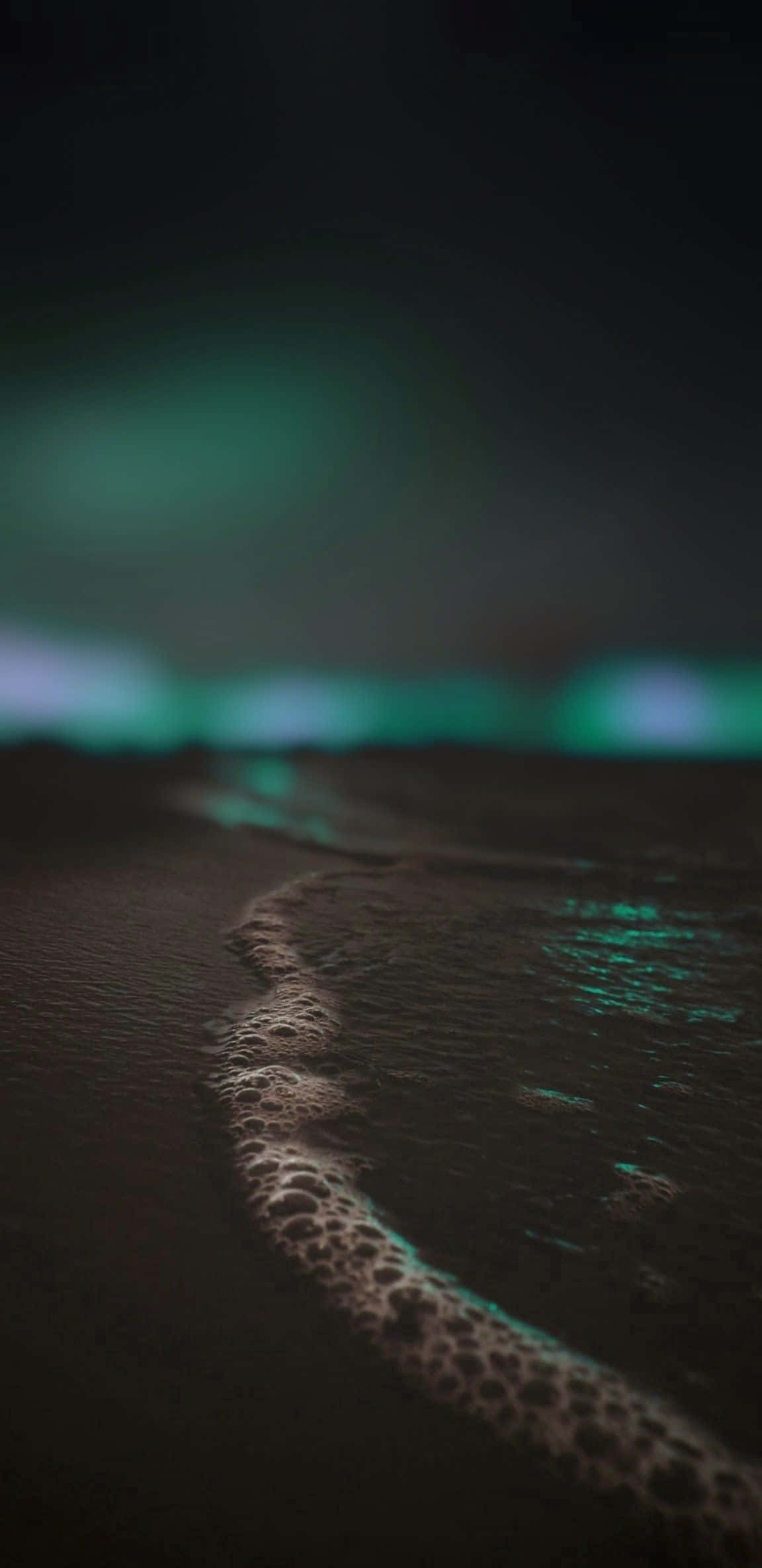 Dark Teal 桌布 壁紙 — 夜晚黑暗的海灘，發光的綠色北極光反射在濕沙和泡沫波浪中。