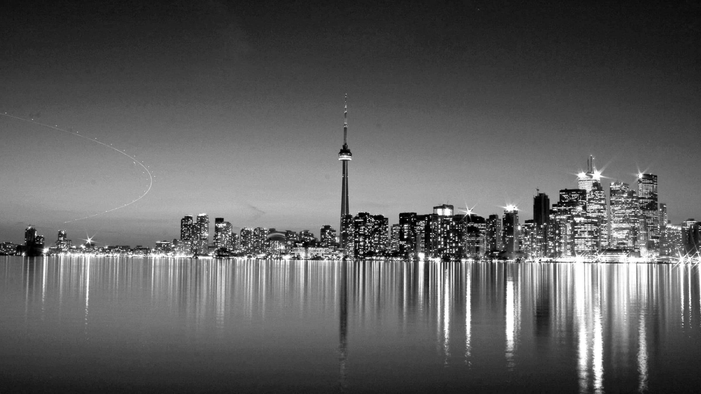 Black And White Cityscape 桌布 壁紙 — 夜晚黑白城市天際線，燈火通明的摩天大樓和高塔倒映在平靜的水面上。