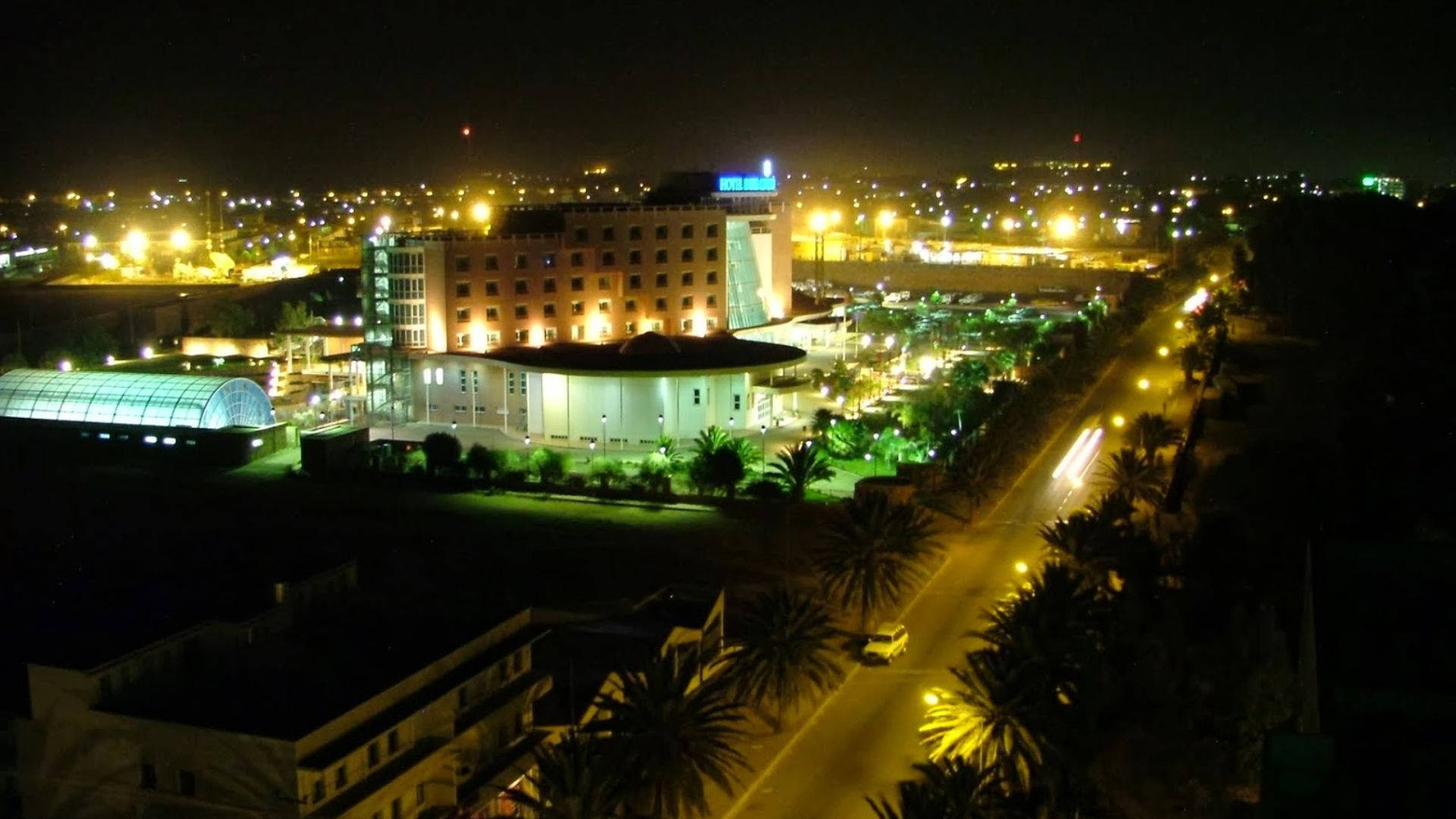 Eritrea 桌布 壁紙 — 夜景城市景觀，特色是燈火通明的飯店綜合體、棕櫚樹和帶有光跡的道路。