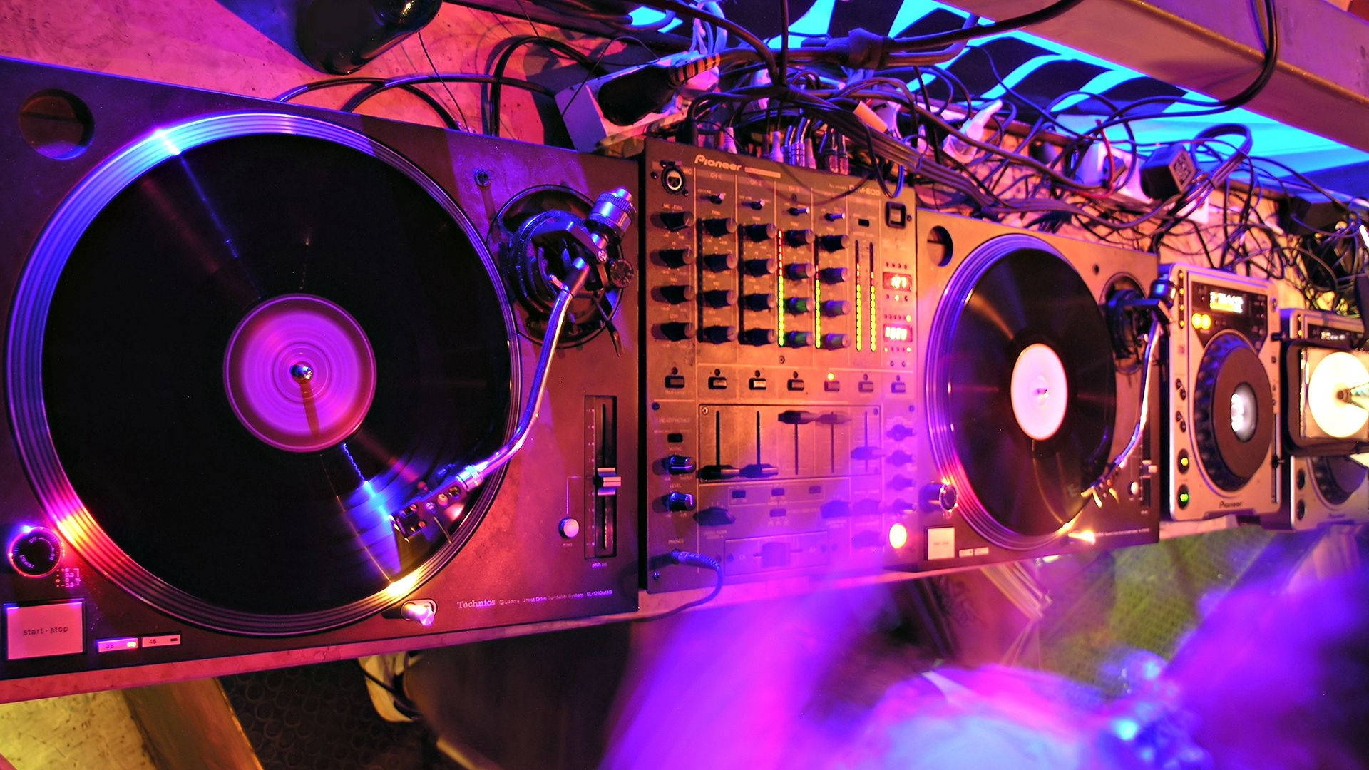 DJ 桌布 壁紙 — 夜總會中帶有旋轉唱盤和發光紫色燈光的DJ設備。