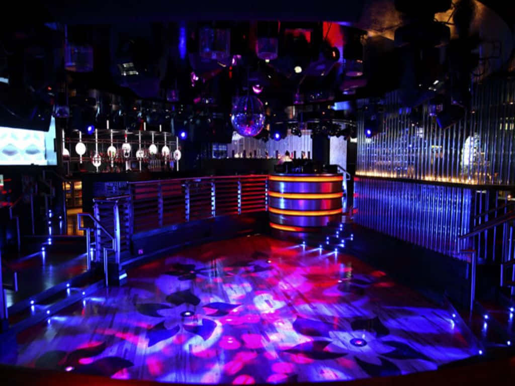 Club Party 桌布 壁紙 — 夜總會舞池沐浴在脈動的紫色和藍色燈光中，頭頂有迪斯科球，背景是發光的酒吧。