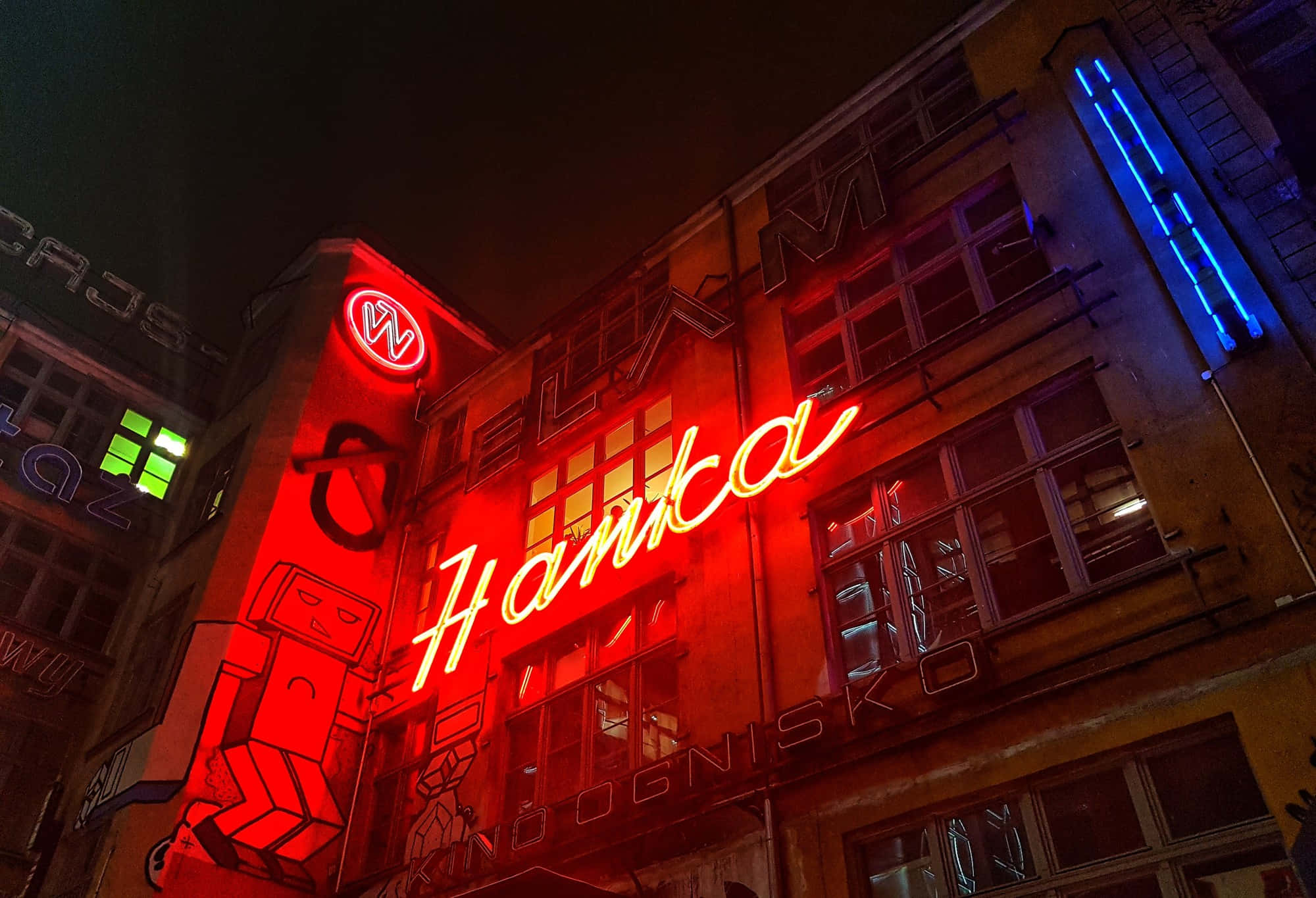 Red Light District 桌布 壁紙 — 夜間，一個寫著「Hanka」的鮮紅色霓虹燈牌在風化的城市建築外牆上閃耀。