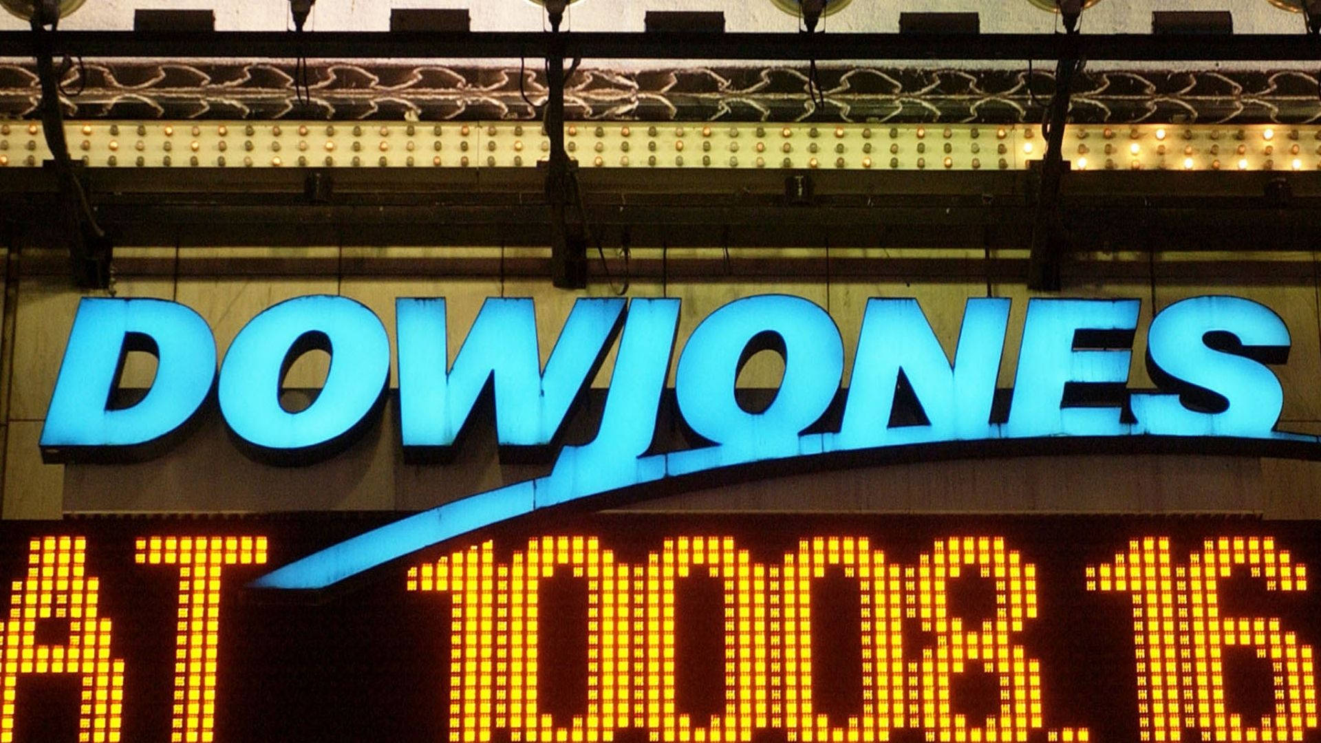 Dow 桌布 壁紙 — 夜間，一個發光的藍色道瓊斯標誌位於顯示股票價格的黃色數位跑馬燈上方。