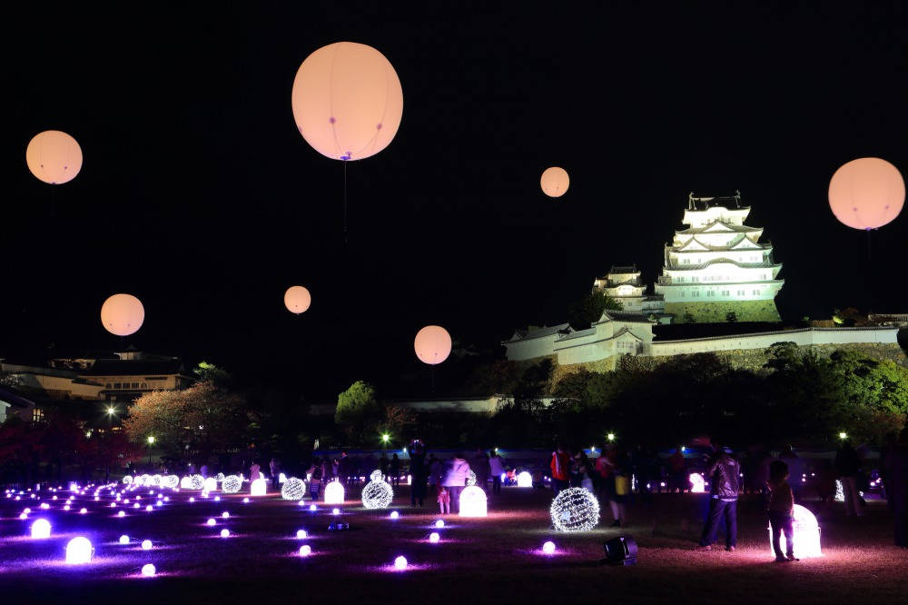Himeji Castle 桌布 壁紙 — 夜間，發光的燈籠漂浮在紫色燈光場地上方，背景是一座燈火通明的城堡。
