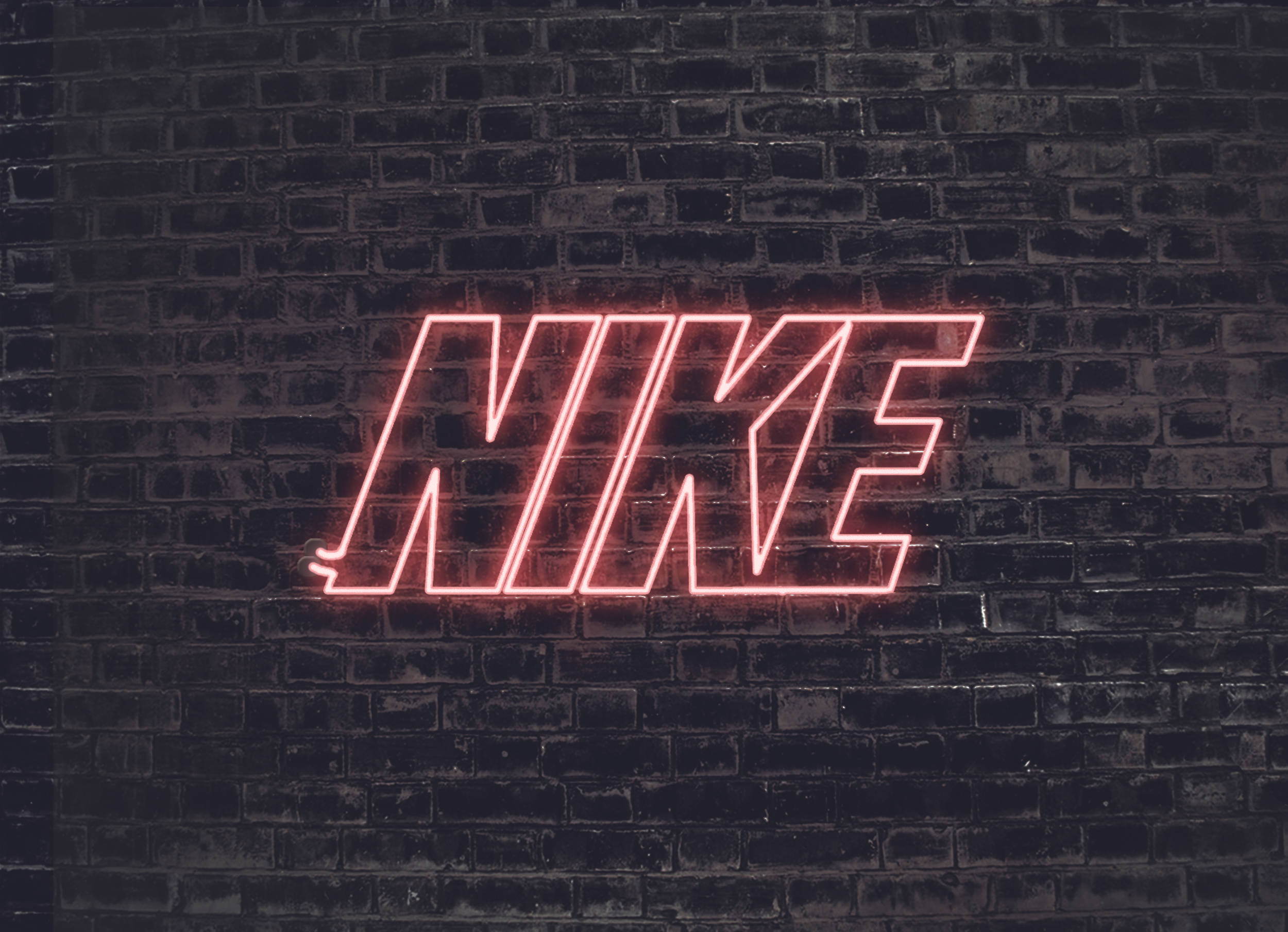 耐吉女孩 桌布 壁紙 — 夜間，發光的紅色霓虹燈Nike標誌在深色紋理磚牆上投射出鮮豔的光芒。