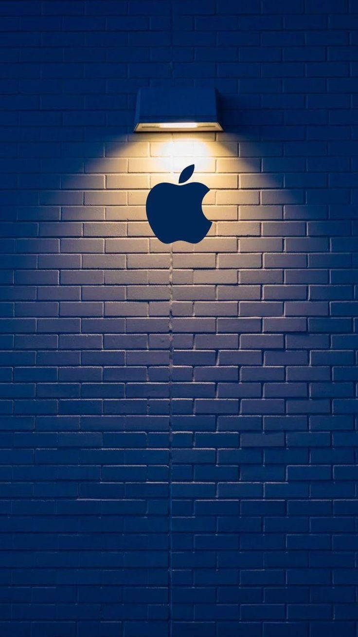 蘋果 桌布 壁紙 — 夜間，聚光燈在深藍色磚牆上投射出發光的Apple標誌輪廓。