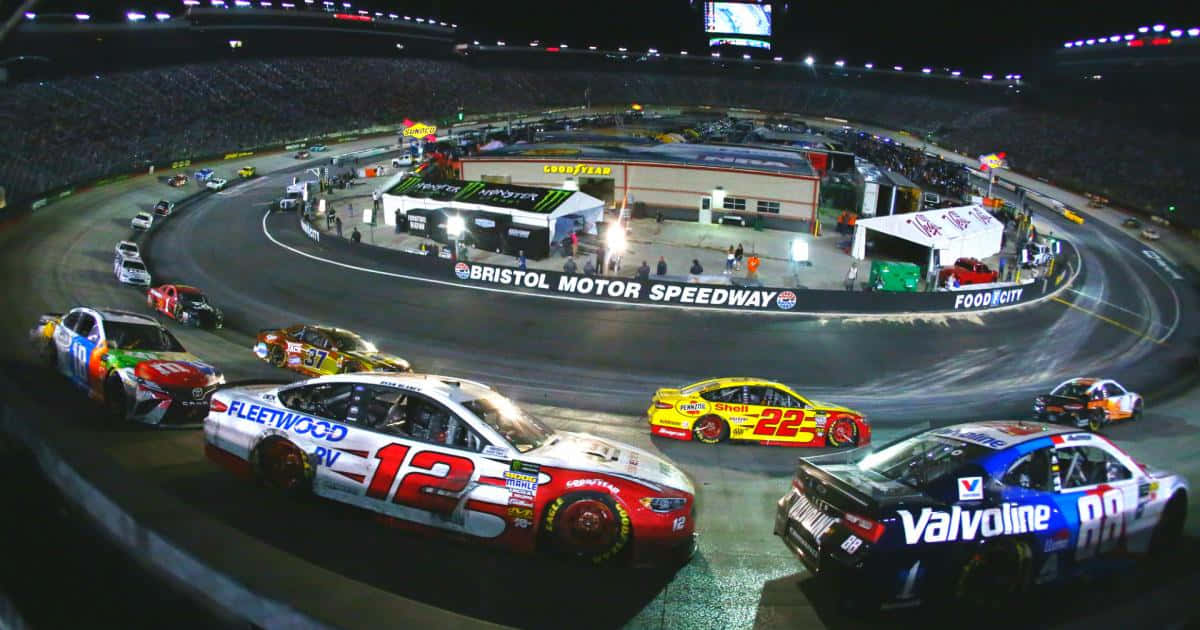 nascar 桌布 壁紙 — 夜間NASCAR賽車在布里斯托爾賽車場的體育場燈光下，在明亮照明的橢圓形賽道上呼嘯而過。