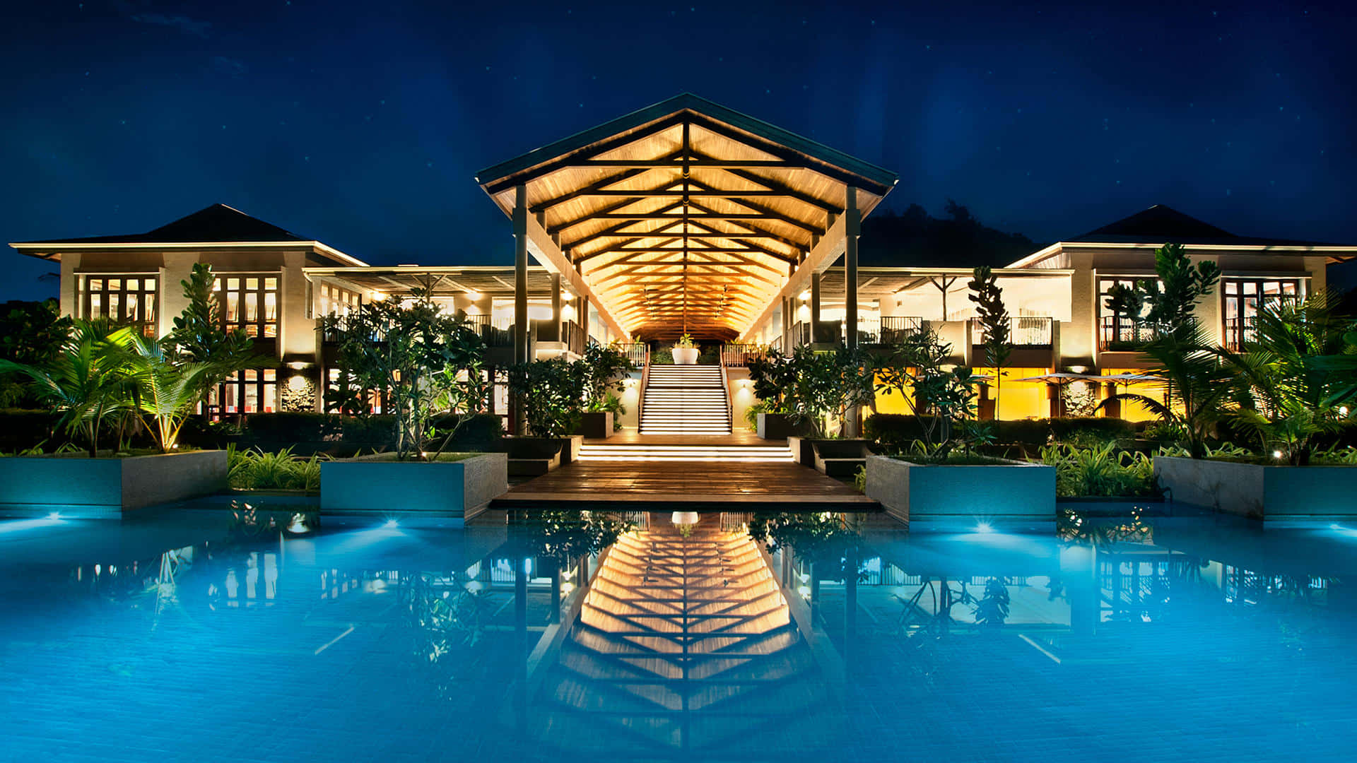 Hotel 桌布 壁紙 — 夜間一個宏偉的熱帶度假村，有一個發光的游泳池，反射著星空和燈火通明的木製亭子。
