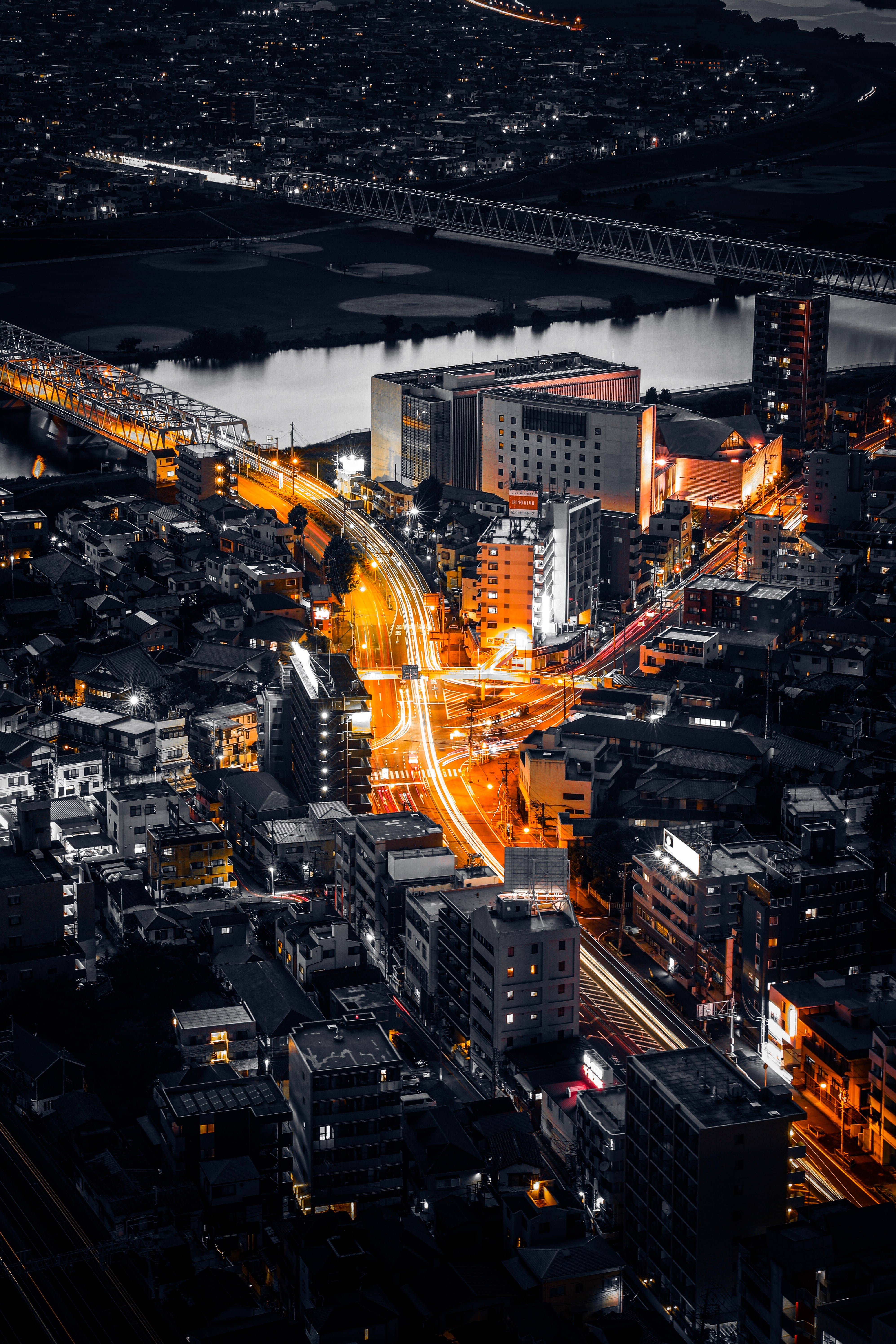 日本 桌布 壁紙 — 夜間充滿活力的城市鳥瞰圖，交通流動在密集的城市建築中蜿蜒，留下發光的橙色光跡。