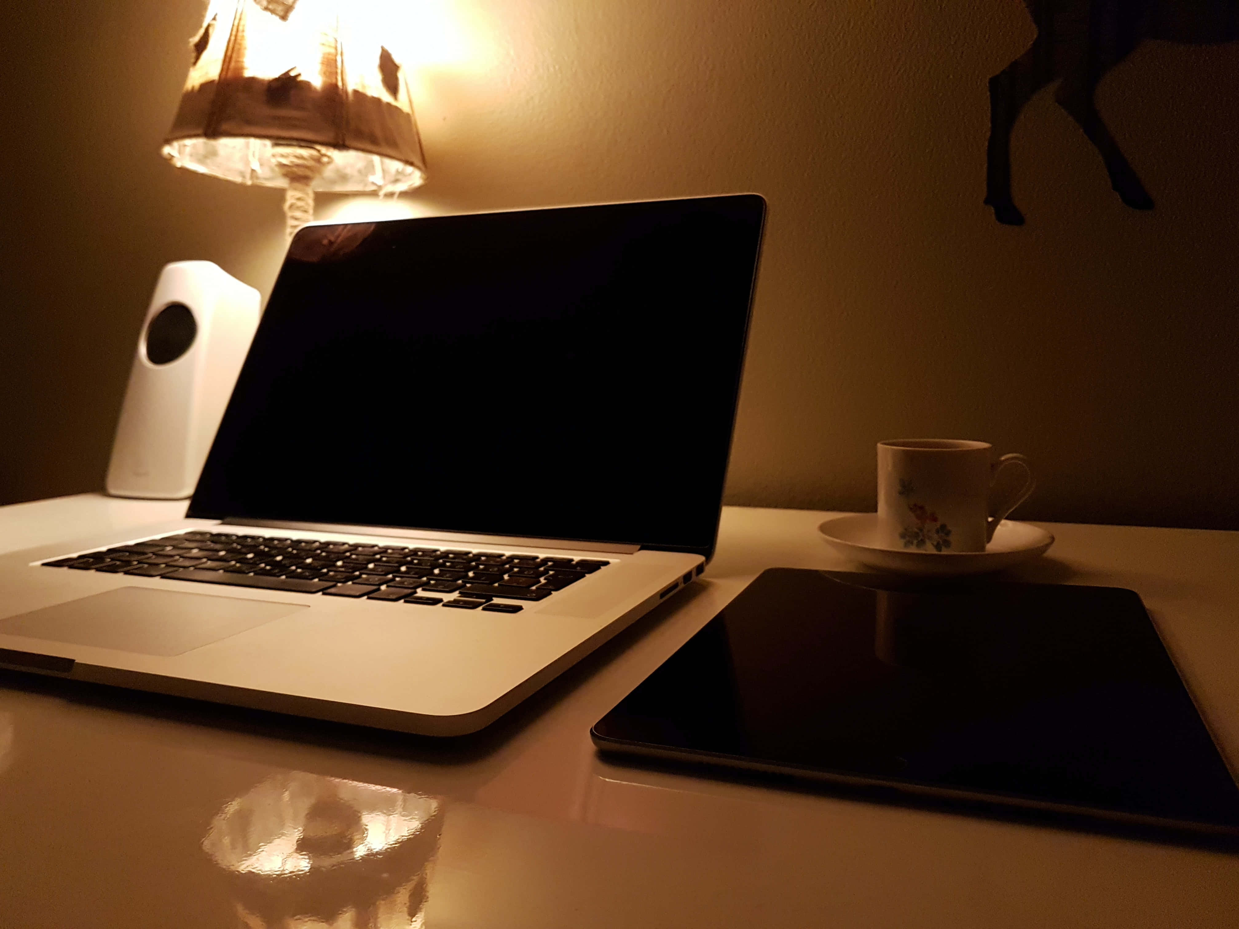 美學 MacBook 壁紙 桌布 壁紙 — 夜間在發光的燈下，溫暖照亮的桌子上有筆記型電腦、平板電腦和花卉杯子。