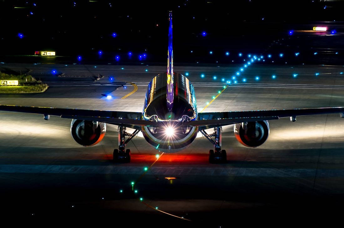 LED 桌布 壁紙 — 夜間在黑暗的機場停機坪上，一架商用客機的後視圖，發出明亮的光芒。