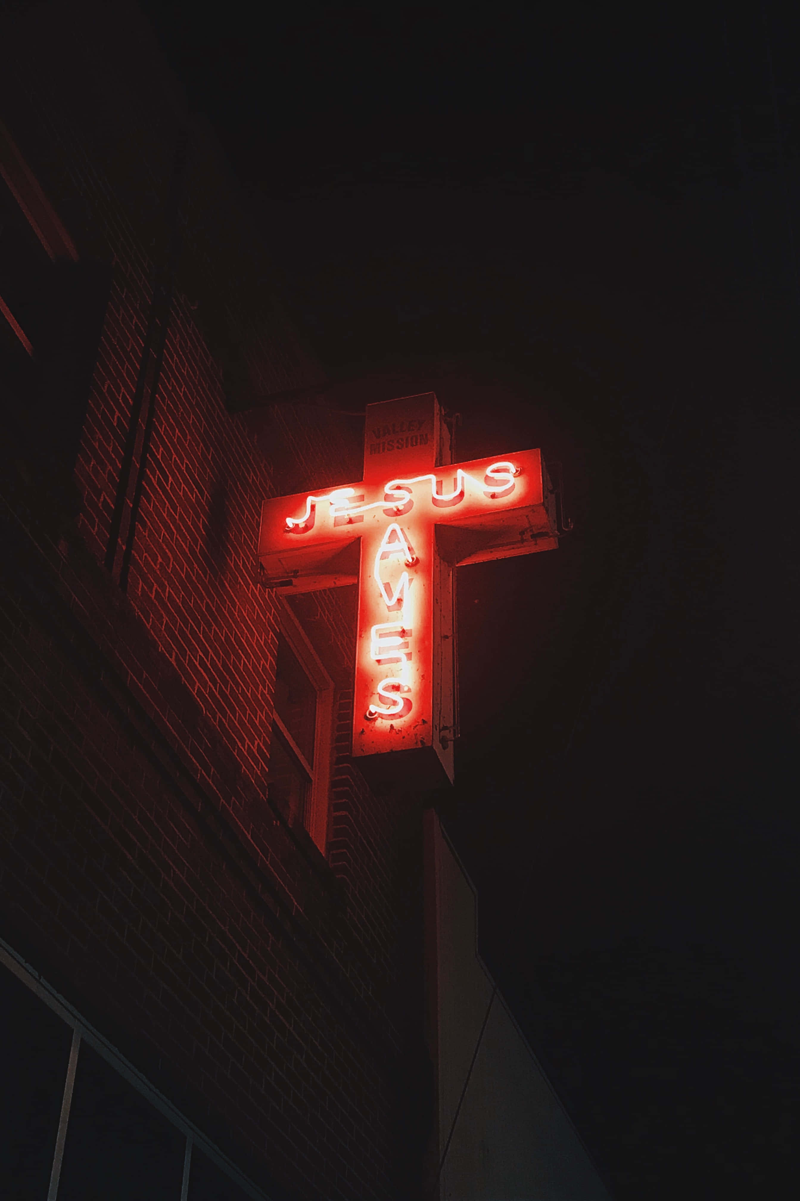 Jesus Saves 桌布 壁紙 — 夜間安裝在磚砌建築物上，一個發光的紅色霓虹十字標誌，上面寫著「JESUS SAVES」。