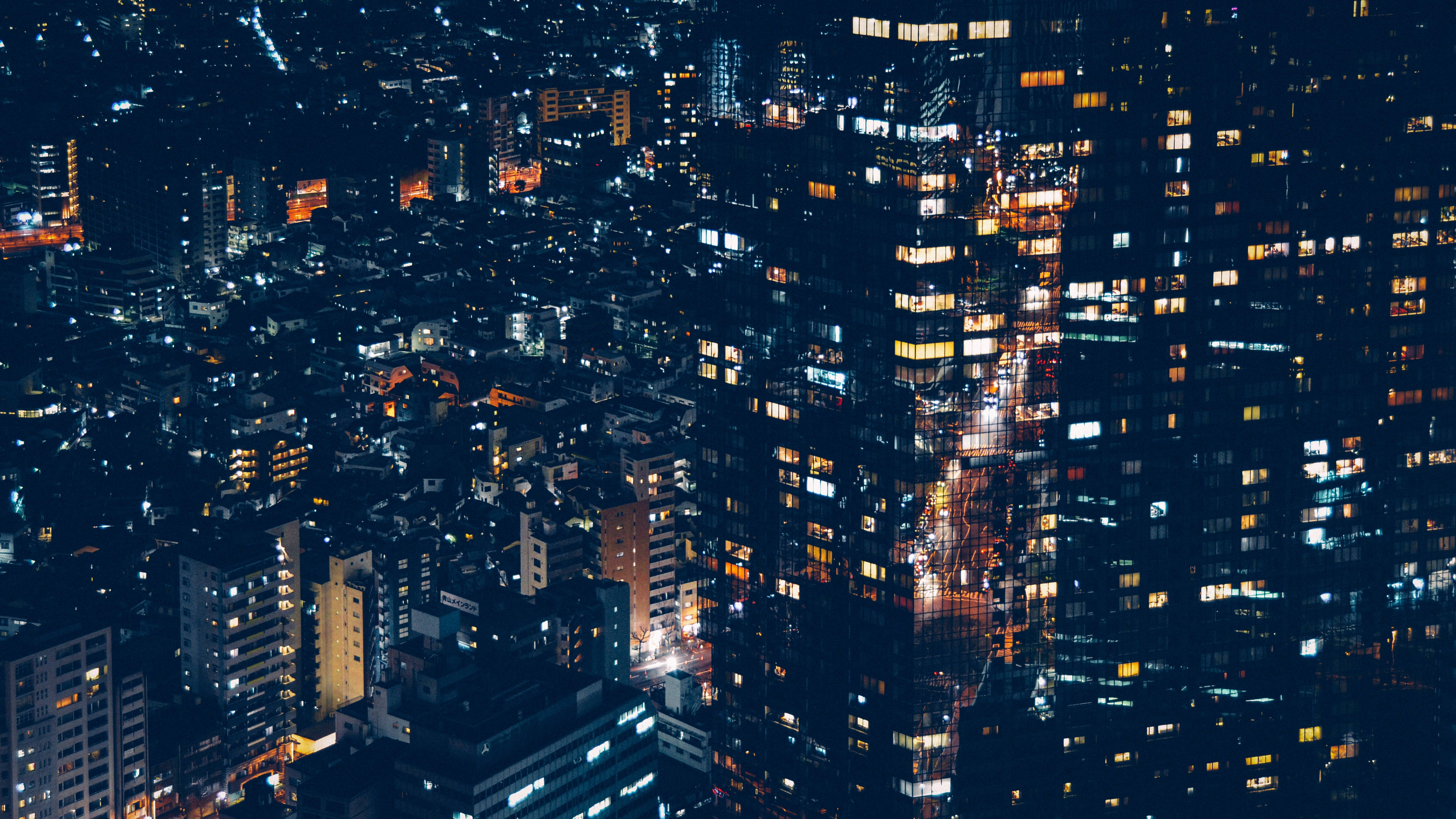 日本 桌布 壁紙 — 夜間密集城市的鳥瞰圖，發光的窗戶和明亮的街道創造出充滿活力的城市掛毯。