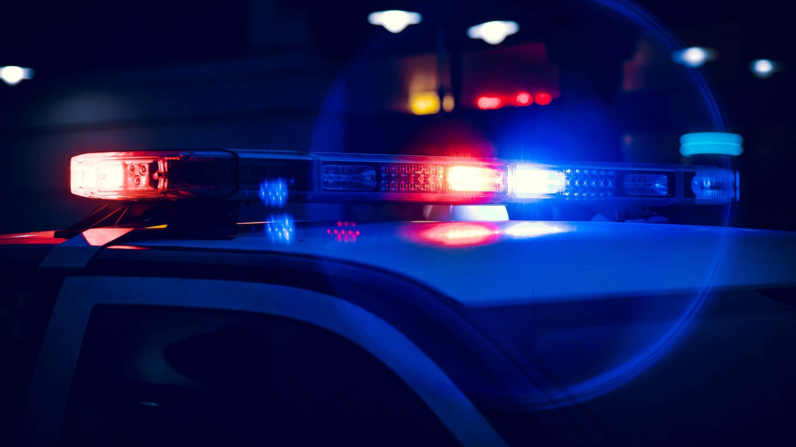 Law Enforcement 桌布 壁紙 — 夜間巡邏車車頂上閃爍的紅色和藍色警燈特寫，帶有鏡頭光暈。