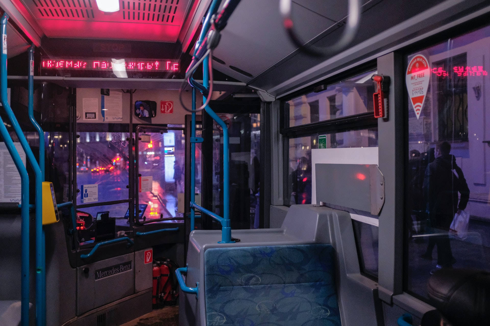 Bus 桌布 壁紙 — 夜間巴士內部，紅色霓虹燈在潮濕的窗戶和空藍色圖案座椅上反射。