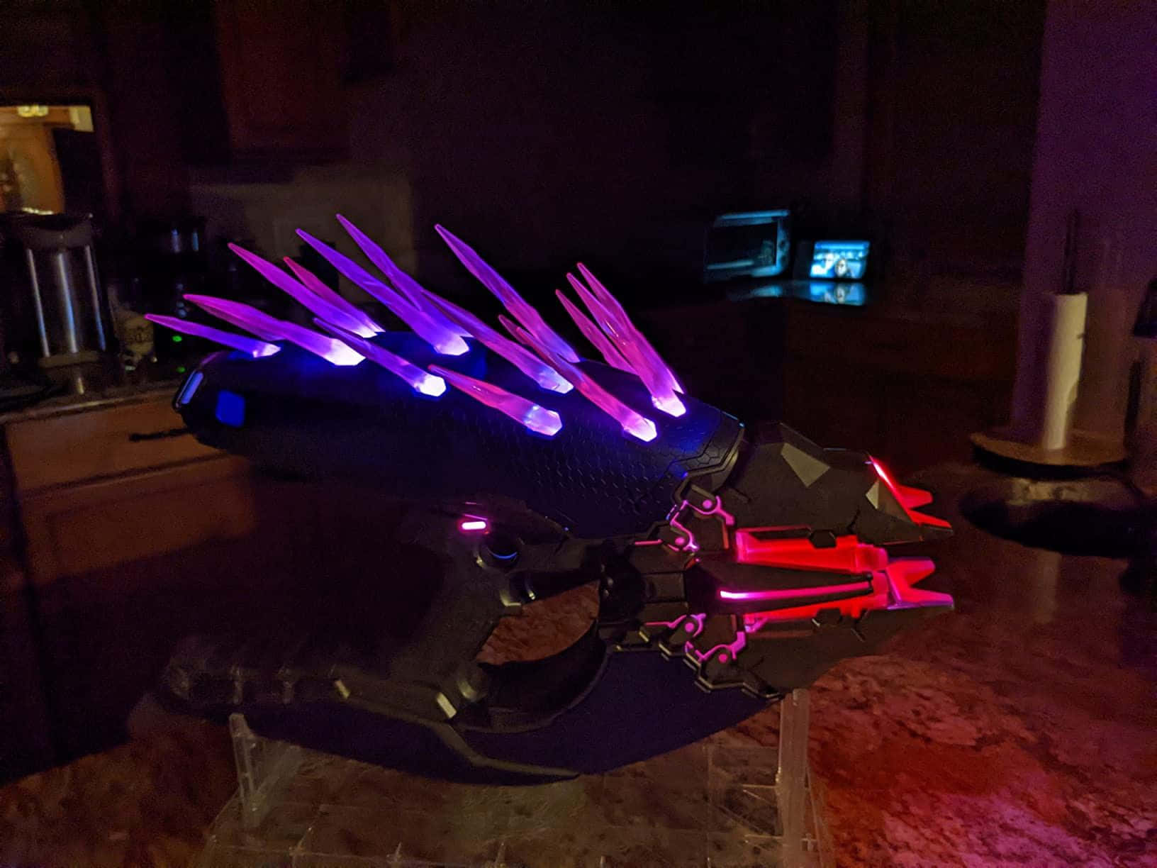 Halo Needler 桌布 壁紙 — 夜間廚房檯面上展示的發光紫色和紅色未來武器，帶有尖刺燈光。