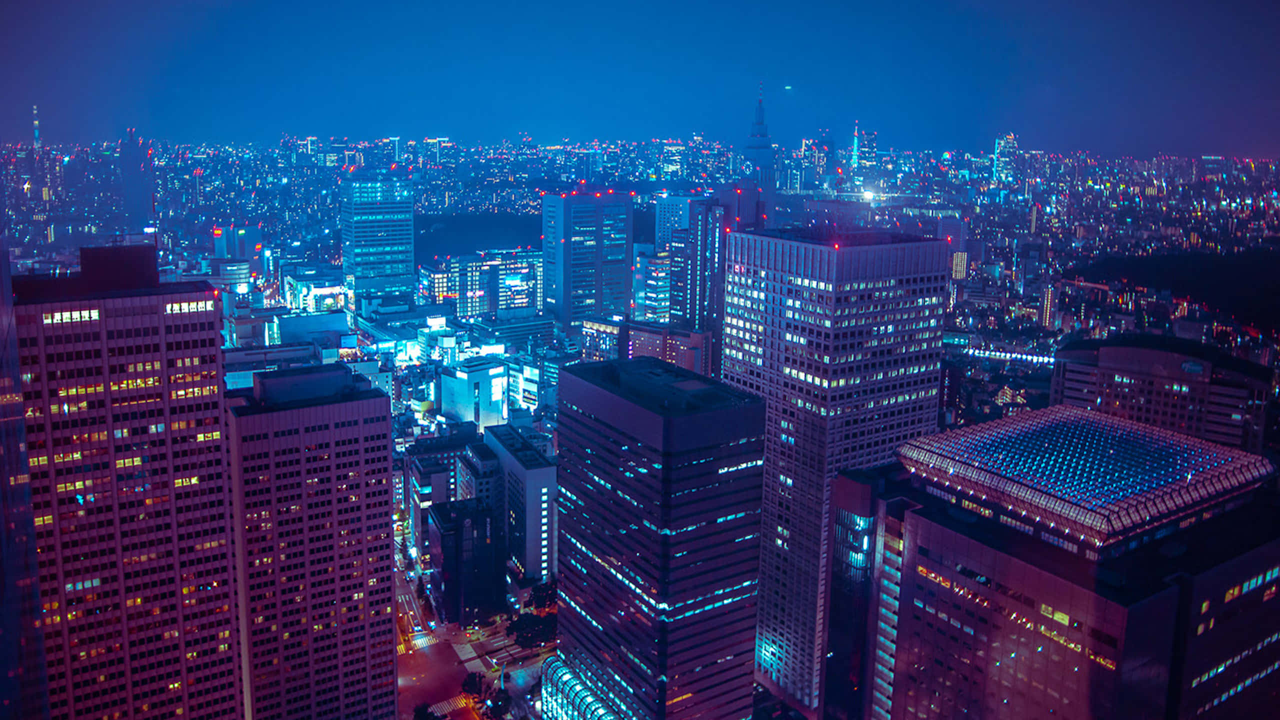 日本 桌布 壁紙 — 夜間廣闊城市的鳥瞰圖，閃爍的摩天大樓和充滿活力的霓虹燈照亮了城市景觀。