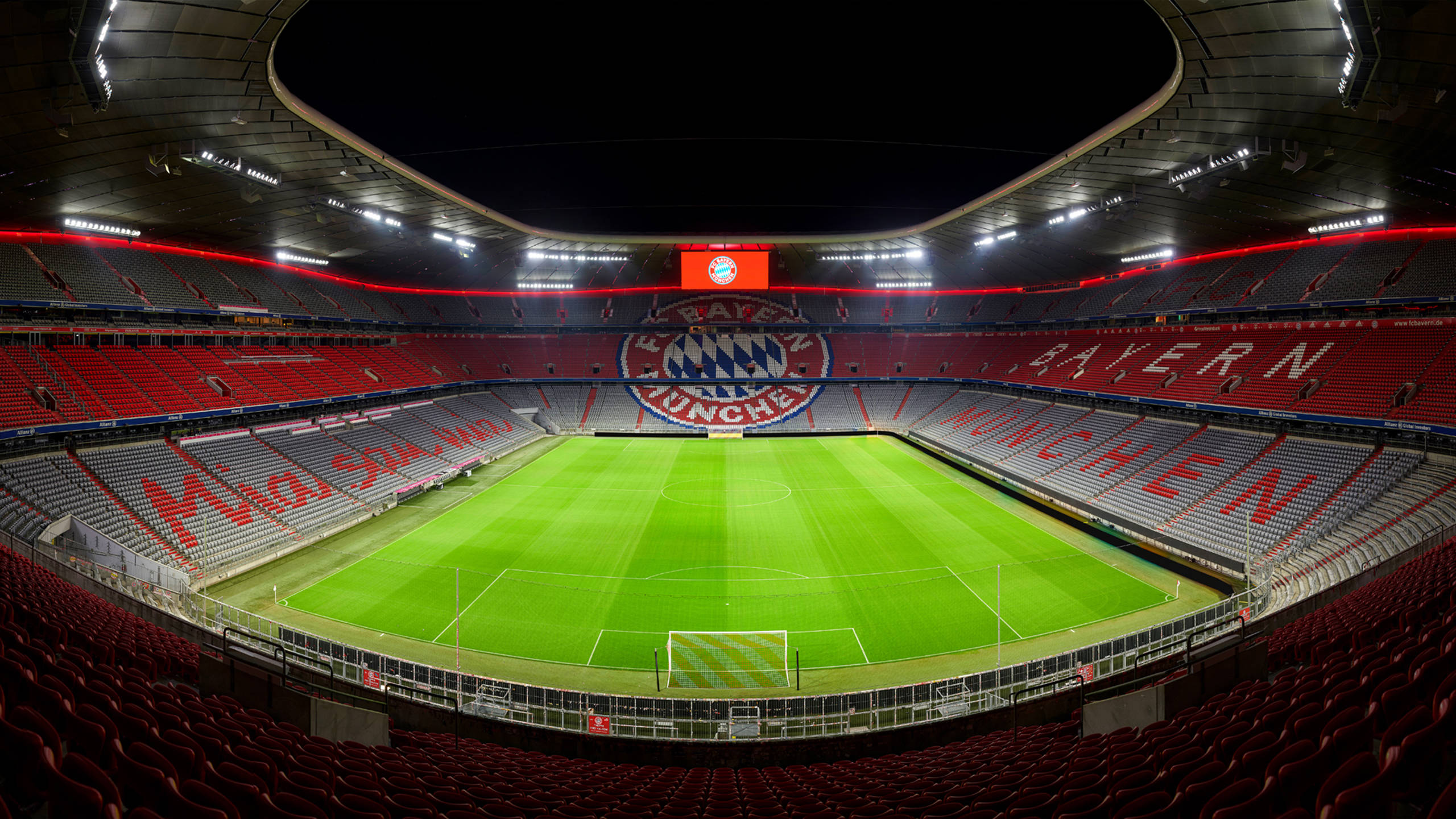 Stadium 桌布 壁紙 — 夜間拜仁慕尼黑球場的廣角視角，展示明亮泛光燈下的翠綠草坪和紅色座位。