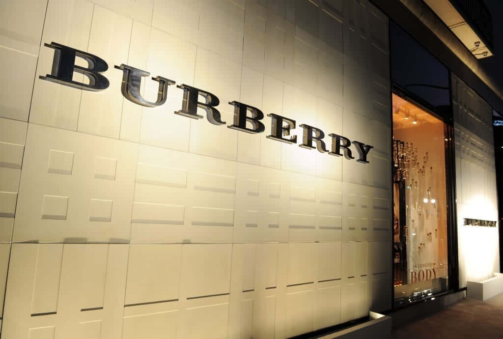 Burberry 桌布 壁紙 — 夜間時尚的 Burberry 商店外牆，帶有發光標誌和帶紋理的白色面板，投射出柔和陰影。