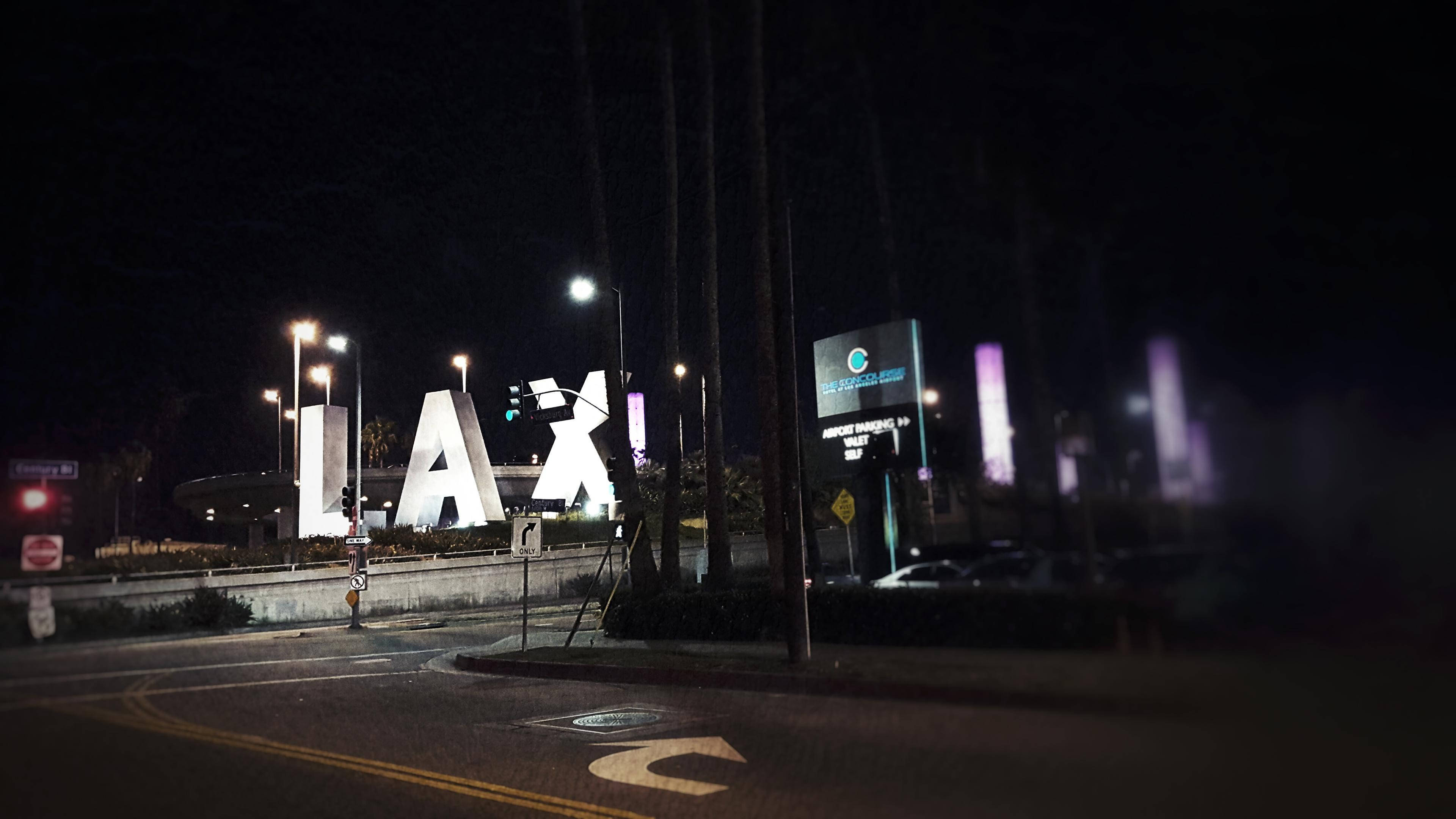 加州 桌布 壁紙 — 夜間景色，發光的LAX機場標誌在黑暗的天空中閃耀，伴隨著街燈和模糊的汽車。