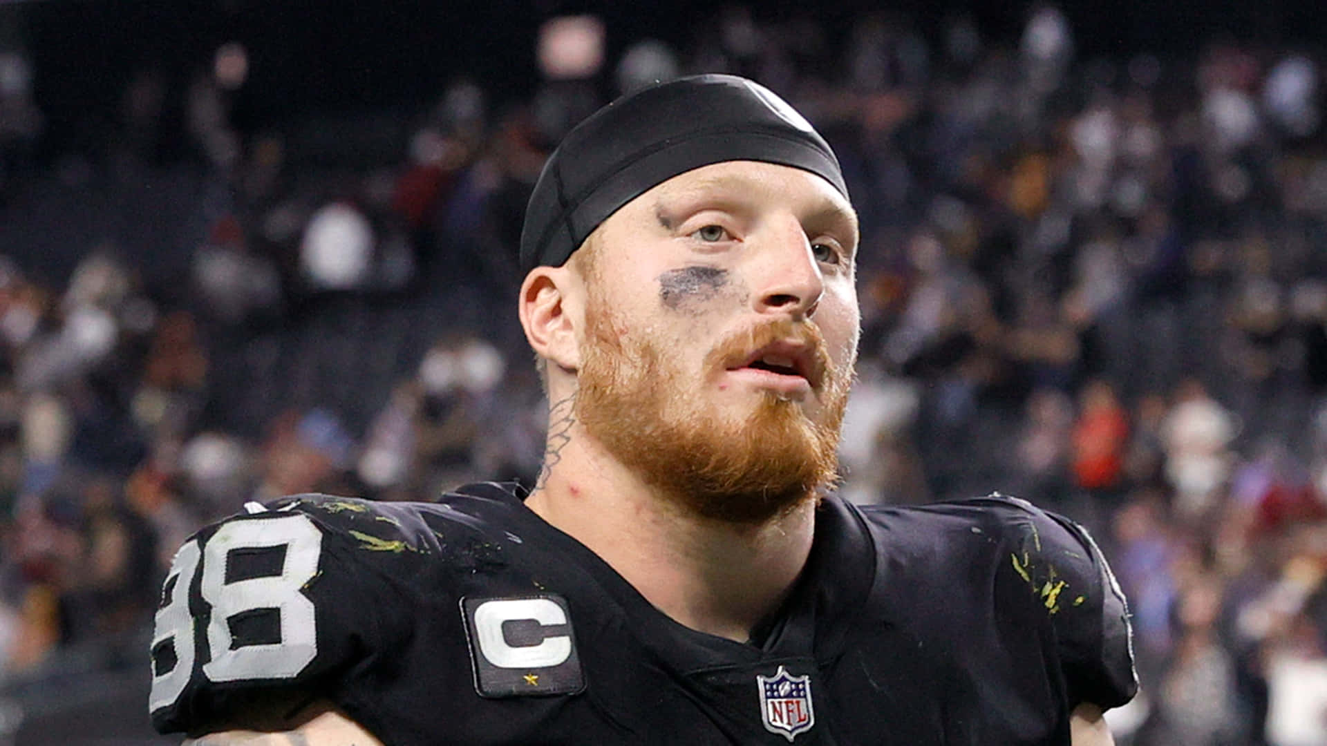 NFL 美式足球 桌布 壁紙 — 夜間比賽中，一位留鬍子的NFL球員身穿黑色球衣（號碼38，隊長臂章）的特寫。