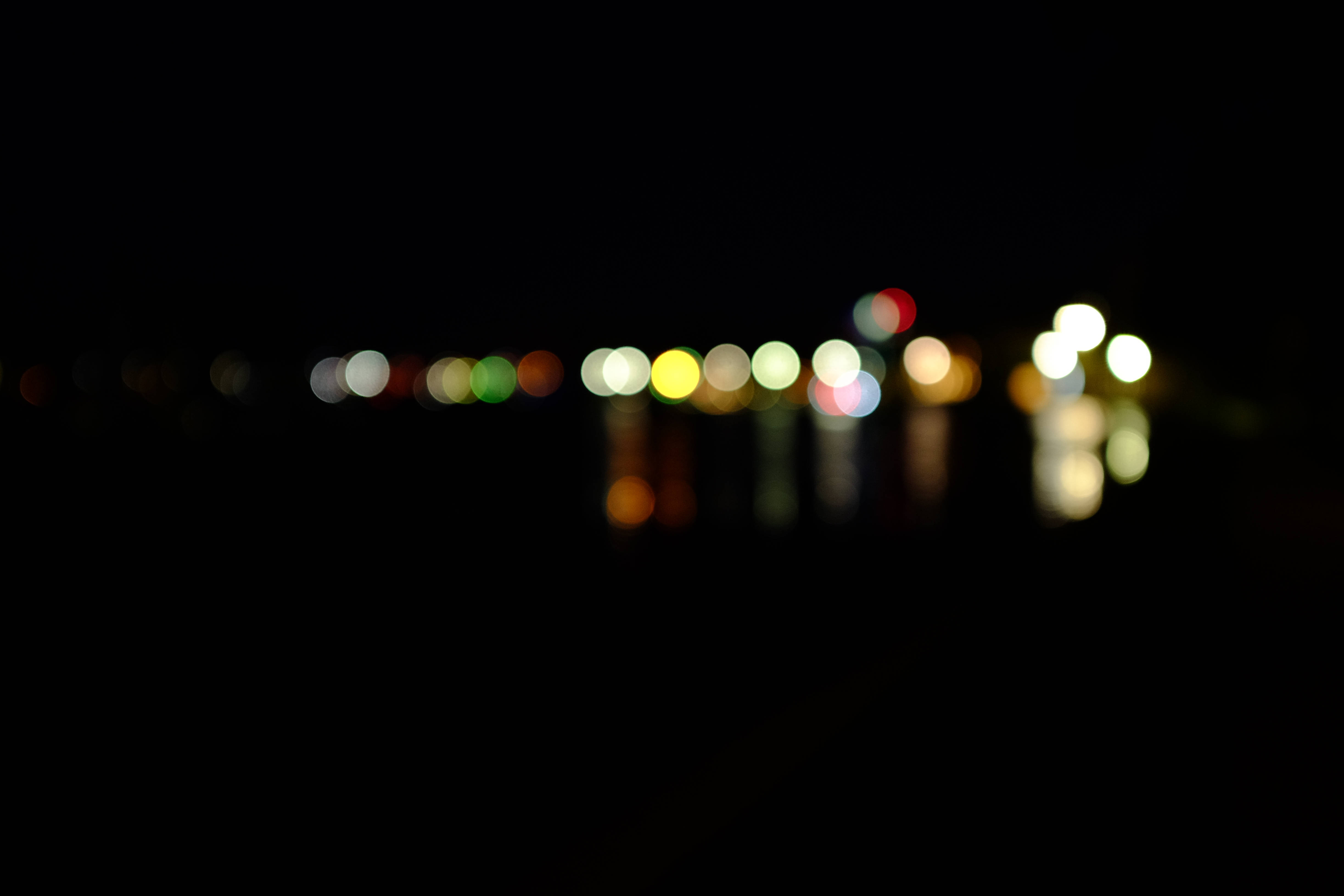 黑色抽象動畫 桌布 壁紙 — 夜間水面上閃爍的散景燈光，在黑暗中營造出夢幻般的抽象光芒。