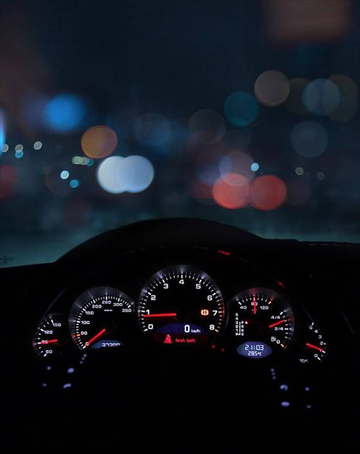 Speed 桌布 壁紙 — 夜間汽車儀表板，紅色指針在散景中模糊的城市燈光映襯下閃爍發光。