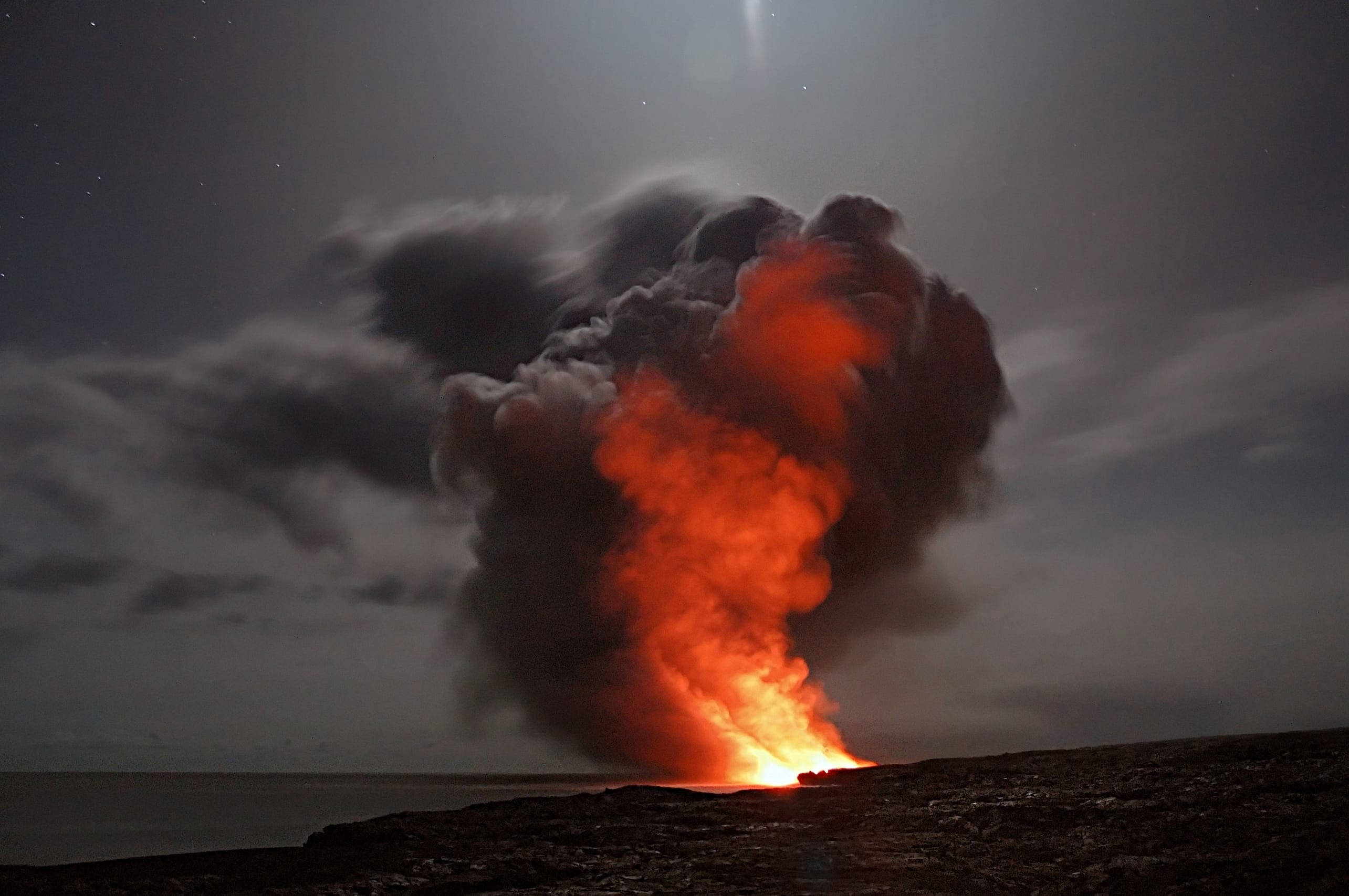 火焰動畫 桌布 壁紙 — 夜間火山爆發，將熾熱的熔岩和灰燼形成的火焰柱送入黑暗海洋地平線之上的星空。