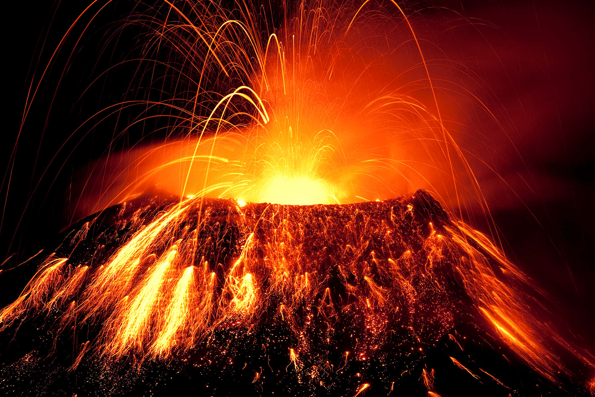 Volcano 桌布 壁紙 — 夜間火山爆發，火橙色熔岩和發光火花射向黑暗的天空。
