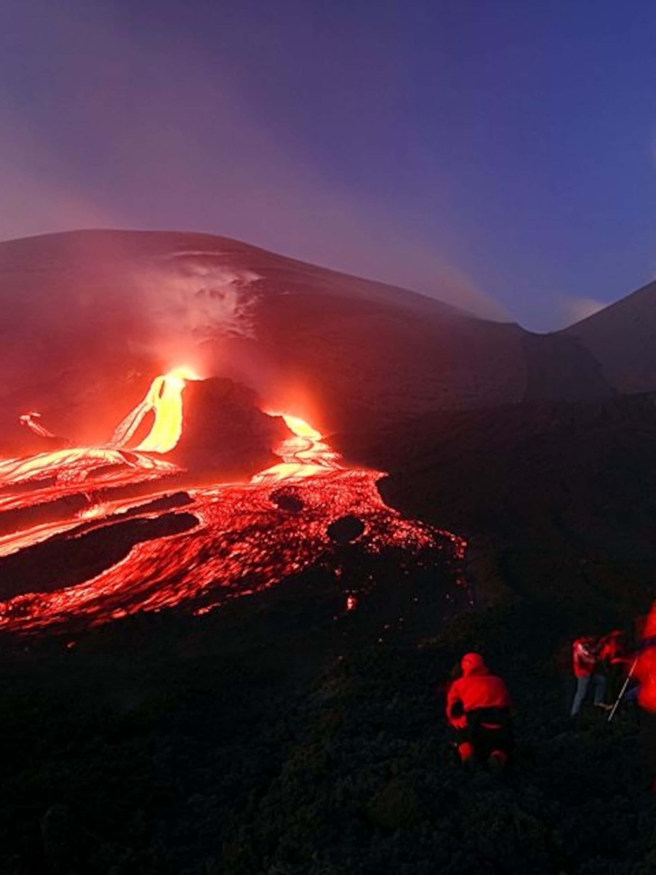 Volcano 桌布 壁紙 — 夜間火山爆發，發光熔岩沿山流下，剪影人物從下方觀看。