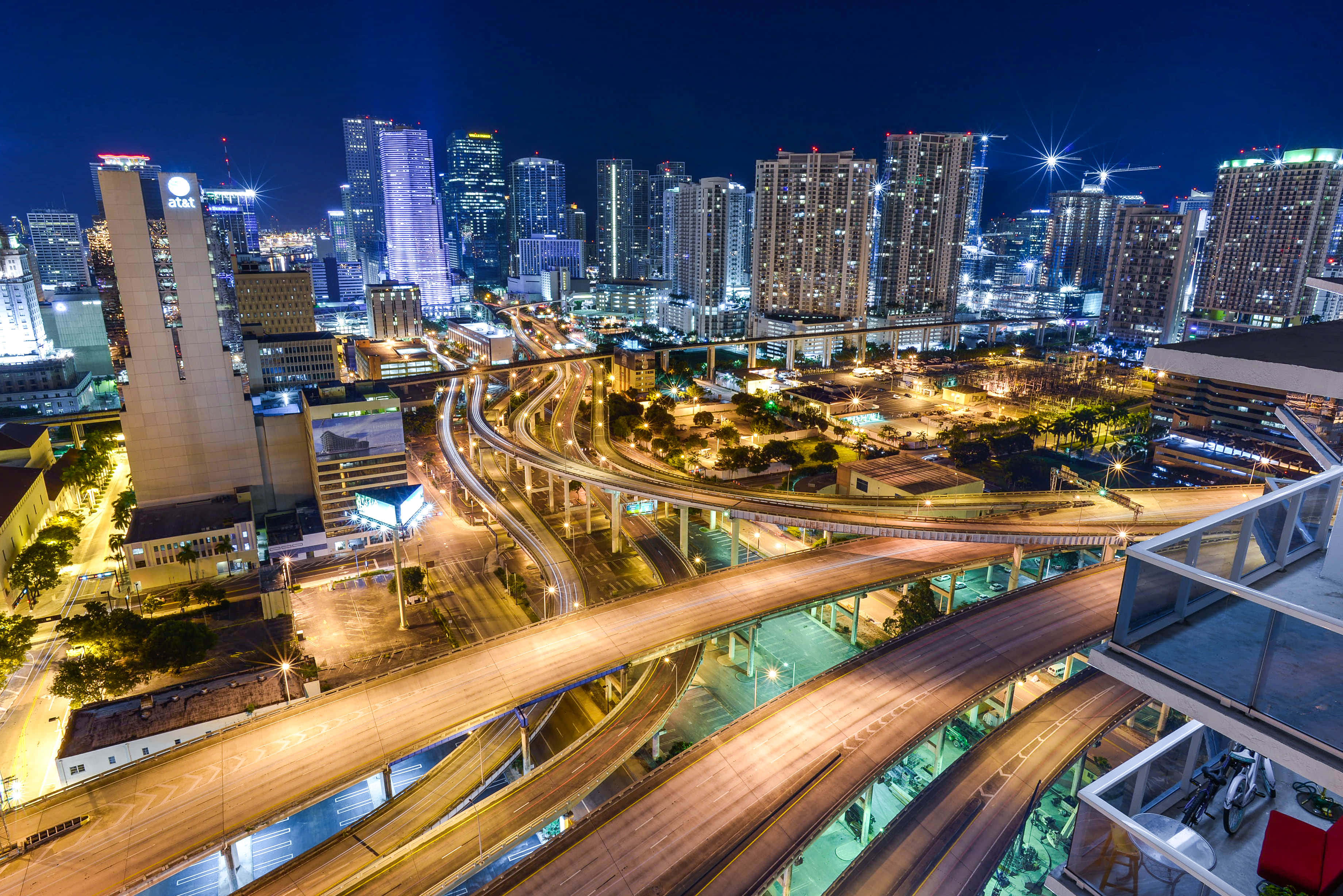 Miami 桌布 壁紙 — 夜間發光城市高速公路交匯處的鳥瞰圖，配有照明摩天大樓和星爆燈光。