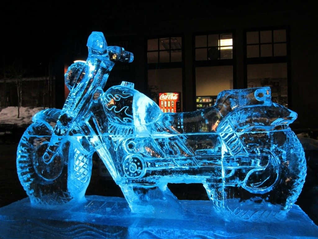 Ice Sculpture 桌布 壁紙 — 夜間發光的藍色冰雕摩托車，地上有雪，後面有亮燈的建築物。