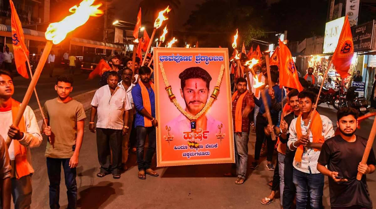 Indian 桌布 壁紙 — 夜間街頭抗議，男子手持燃燒火炬和橙色旗幟，圍繞一個帶有花環和卡納達語文字的大型男子肖像。