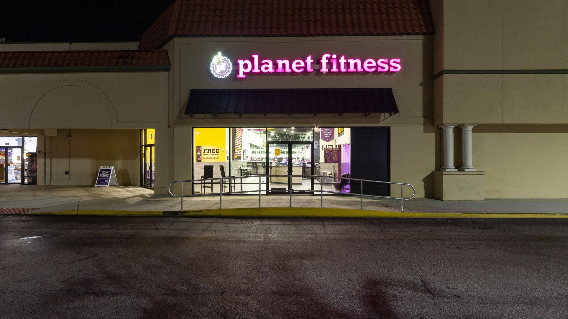 Orange City 桌布 壁紙 — 夜間被明亮粉紅色霓虹燈招牌照亮的Planet Fitness健身房店面，前面有濕瀝青停車場。
