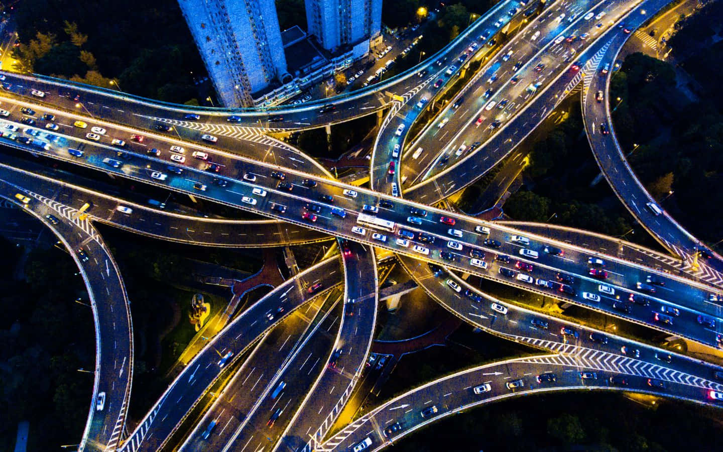 1440x900 桌布 壁紙 — 夜間複雜高速公路交匯處的鳥瞰圖，發光的車燈在彎曲的高架道路上穿梭。