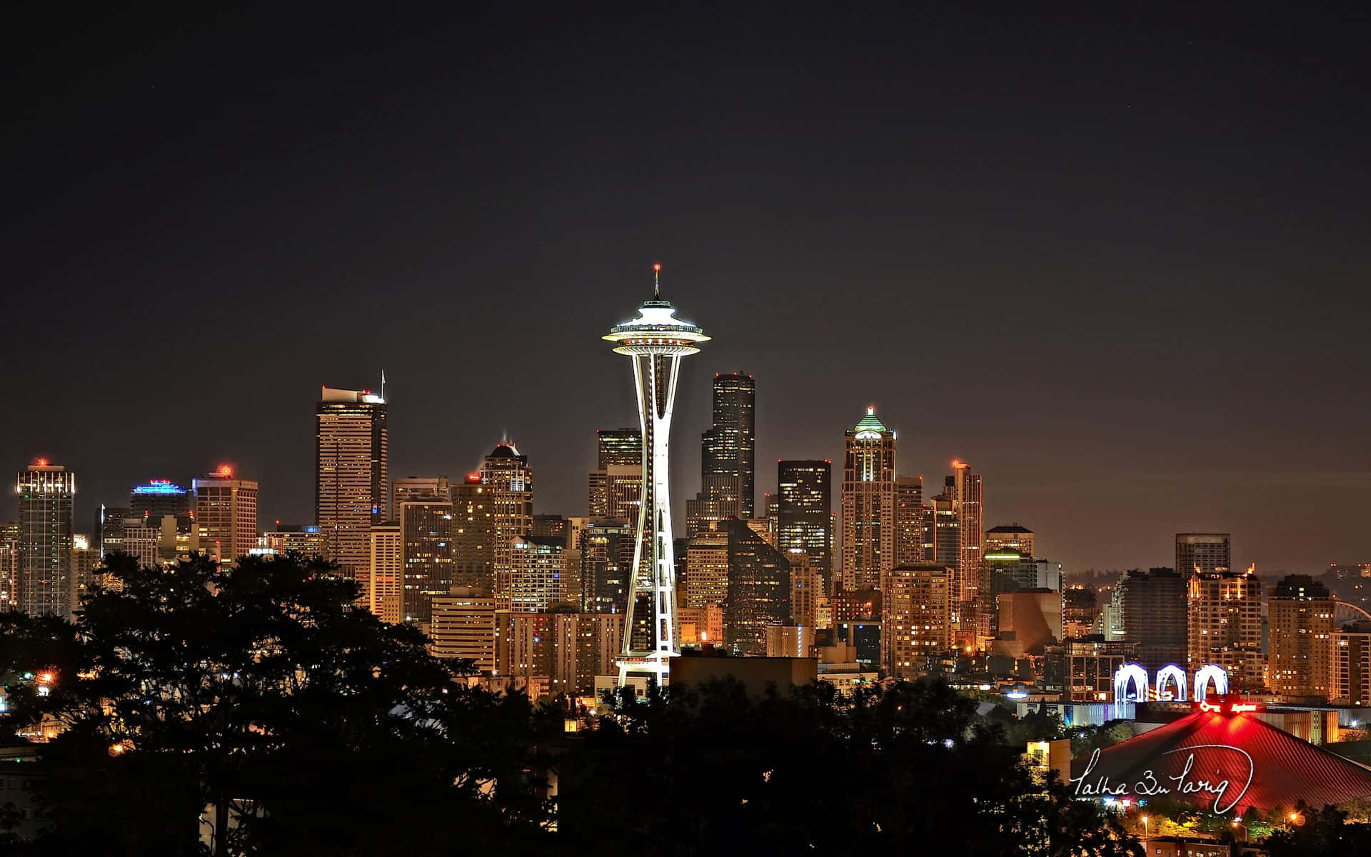 Seattle Washington 桌布 壁紙 — 夜間西雅圖天際線被城市燈光照亮，太空針塔在黑暗的天空中閃耀突出。