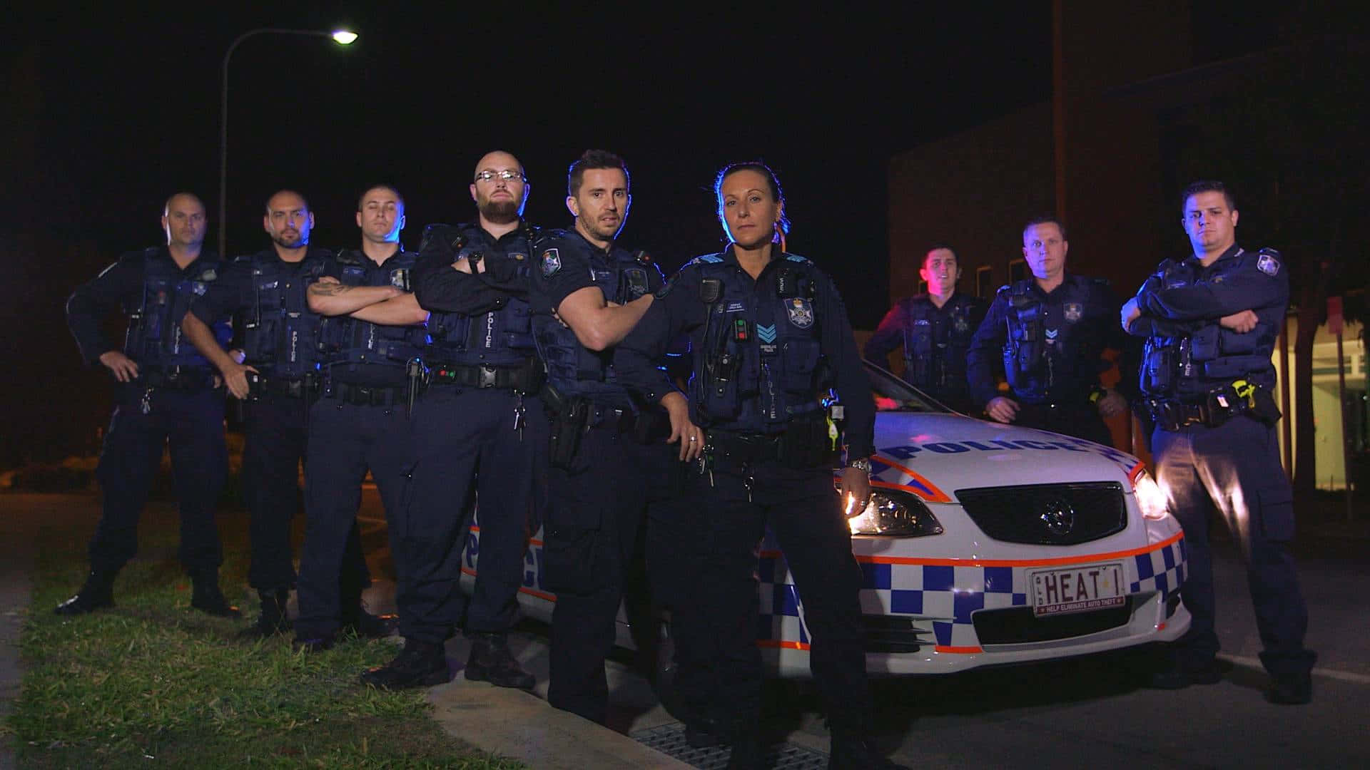 Law Enforcement 桌布 壁紙 — 夜間警察穿著深色制服，在路燈下自信地站在標記的巡邏車周圍。