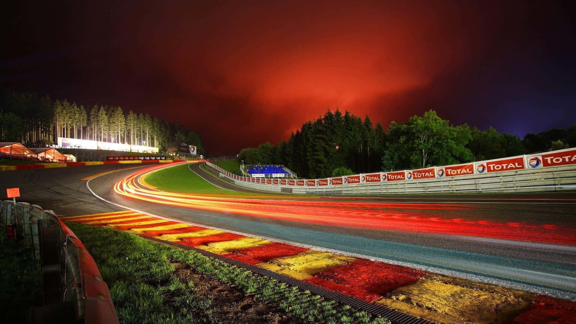 Racing 桌布 壁紙 — 夜間賽道在火紅的天空下蜿蜒，汽車燈光的條紋在瀝青上繪畫。