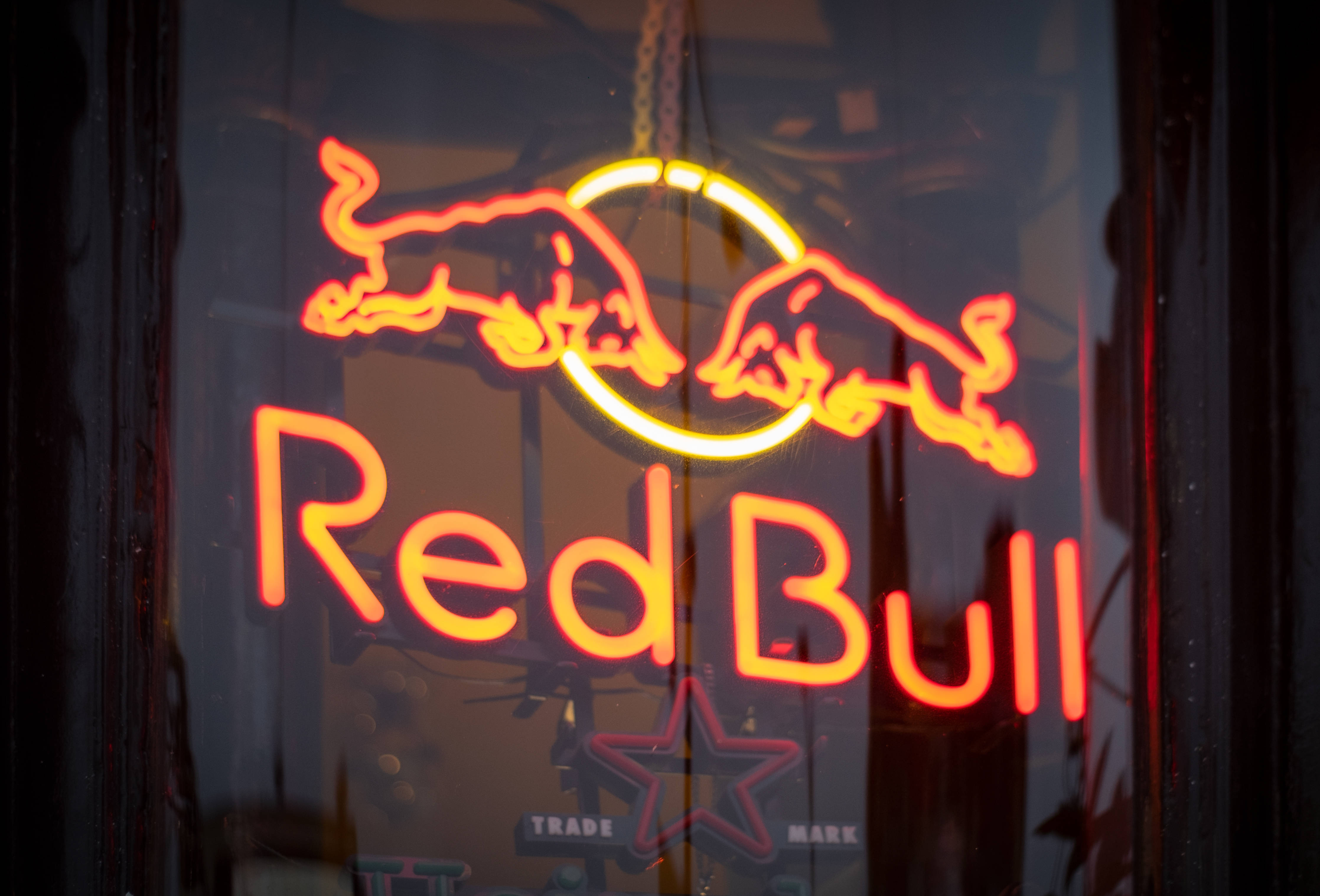 bull 桌布 壁紙 — 夜間透過玻璃窗可見的圓形內兩頭衝鋒的公牛和「Red Bull」文字的發光紅色霓虹燈標誌。